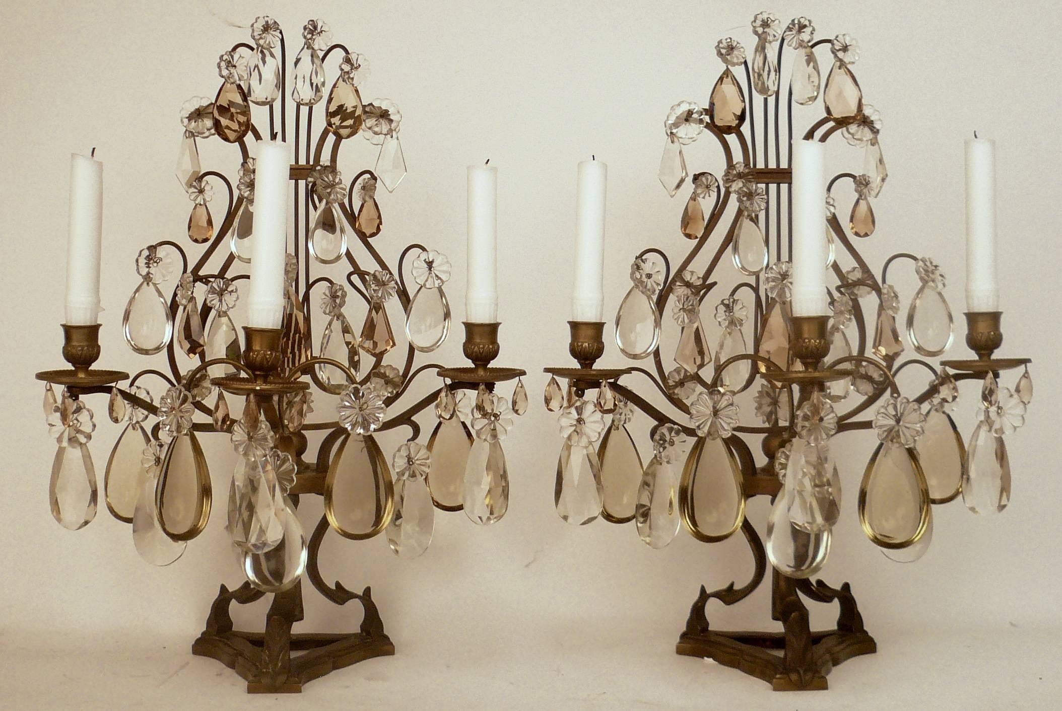 This pair of lyre form patinated bronze lustres feature clear and topaz cut crystal prisms. Originally made for candles, these candelabra may be electrified at no additional cost.
