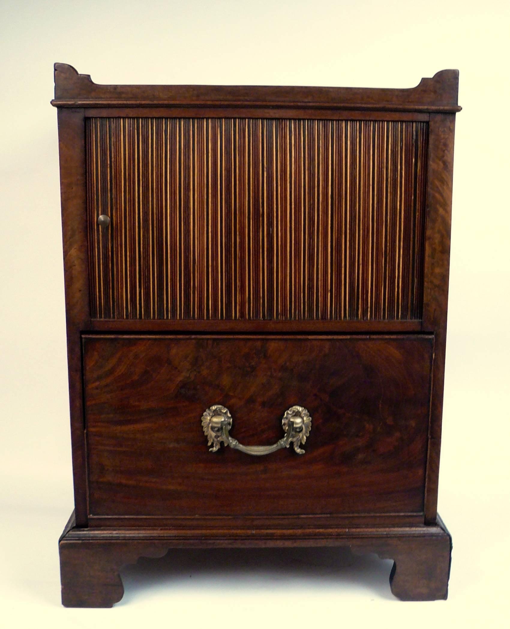 This extra fine quality bedside commode has a lovely old color and patina. It features cut out handles above a plum pudding mahogany top, and a pattered tambour door. The figured mahogany pull out bottom drawer retains its original cast brass