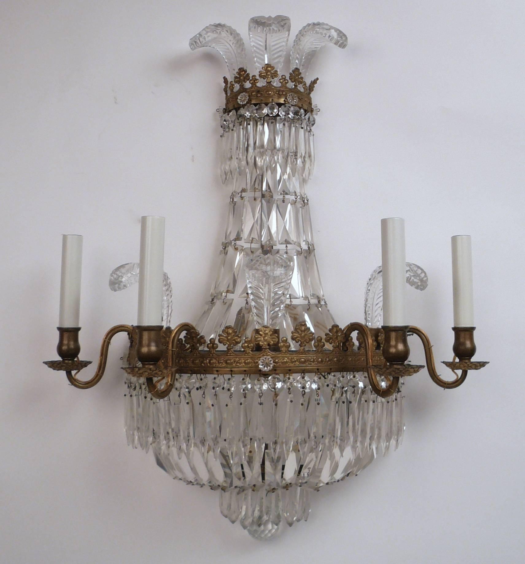 These Hollywood Regency style four light sconces of tent and bag form feature a cut crystal feather corona.
The brass repousse frame incorporates neoclassical motifs and is hung with faceted crystal drops.