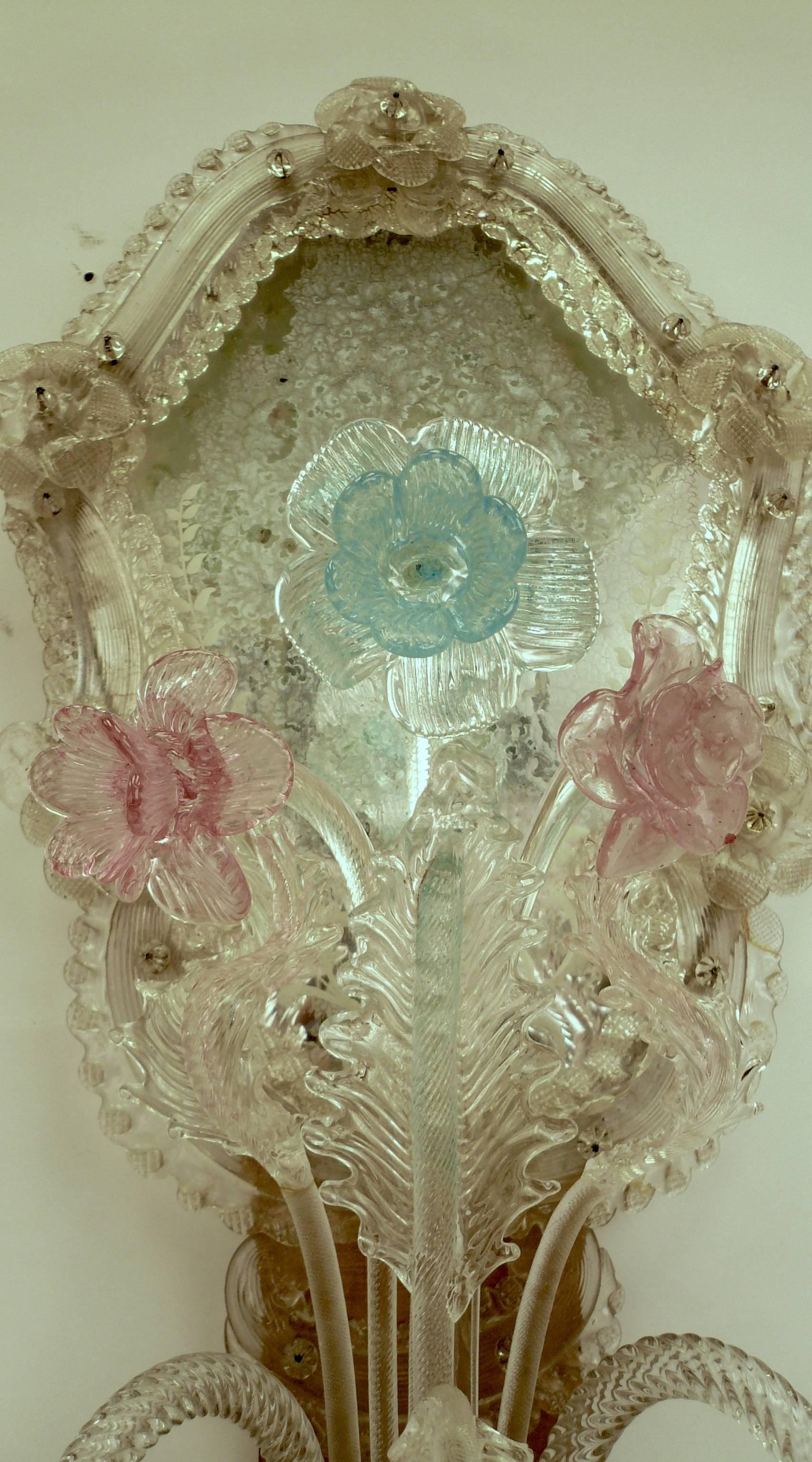 This iconic style of blown Venetian glass has been made on the island of Murano for centuries. The two-arm sconces feature clear, pink, and blue glass floral elements, and mirrored cartouche backs.
