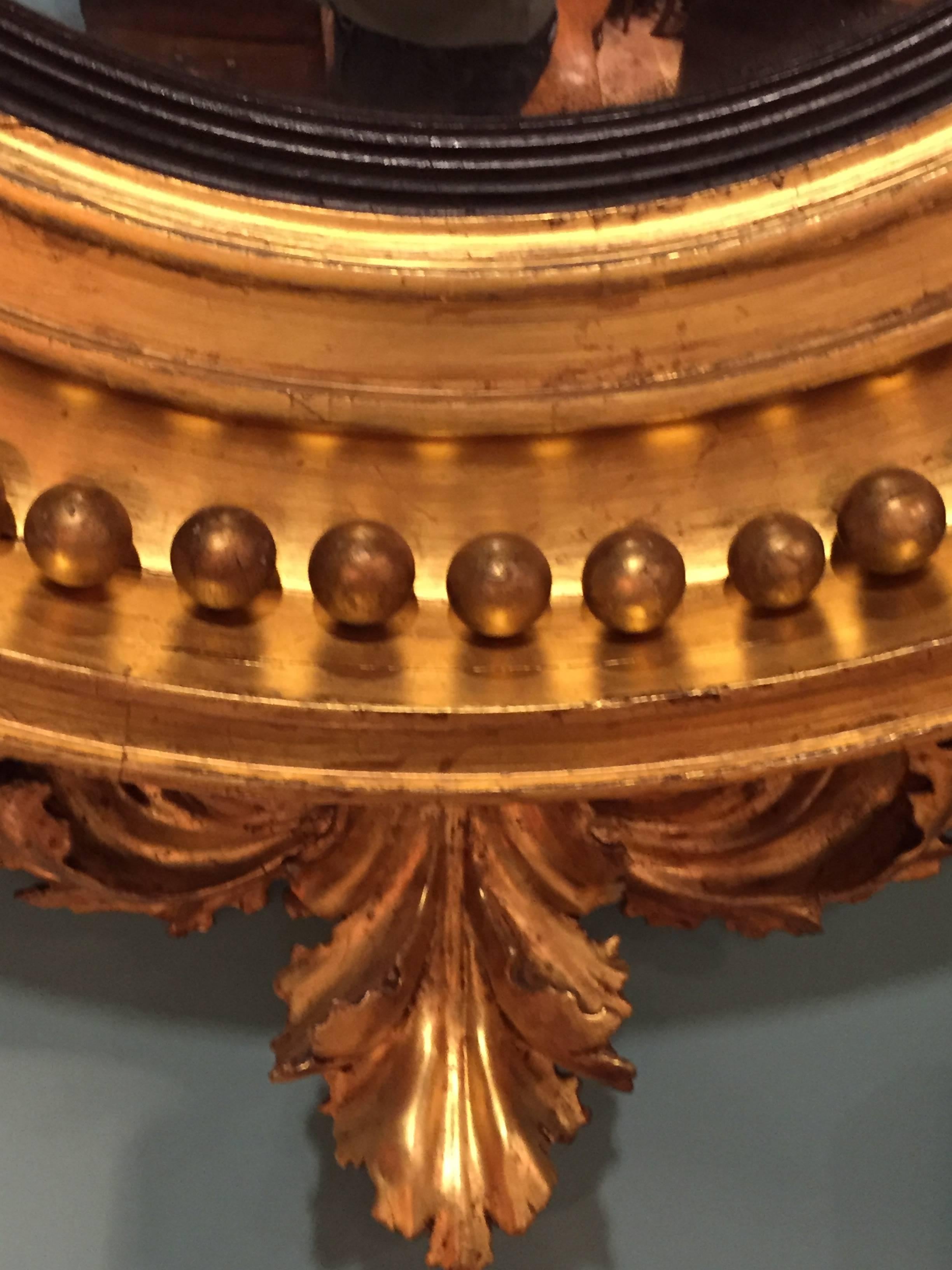 English or American large convex mirror carved of wood with gold gilt finish. Large eagle perched in foliage on top with same foliage continuing at bottom.