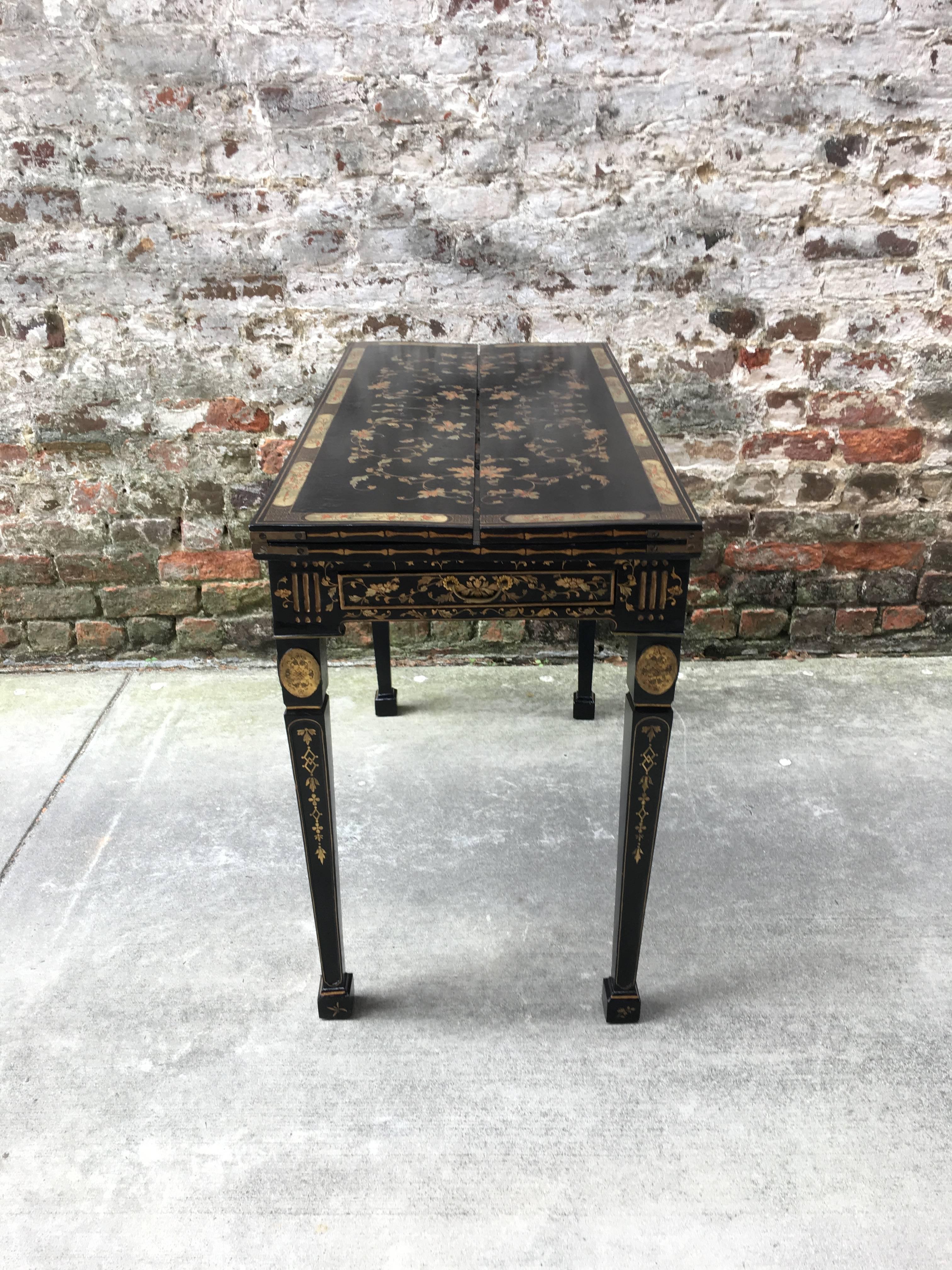 

CHINESE EXPORT LACQUERED GAMING TABLE, CIRCA 1805 in the neoclassical style, with a rectangular top with two hinged leaves opening to a playing surface with chip and candle indentations and a reversible backgammon/chessboard over a storage well