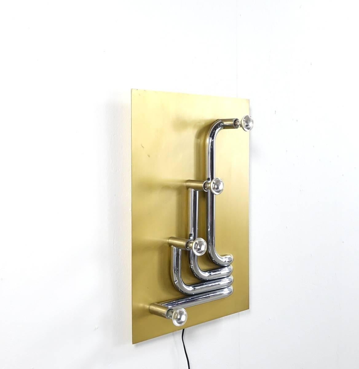 Sculptural wall lamp from the 1970s. Four chrome-plated curved metal tubes are fixed on an aluminium ground. This sculptural lamp is not only beautiful as a wall sculpture, it is also amazing when it gives light. You can hang it in four different
