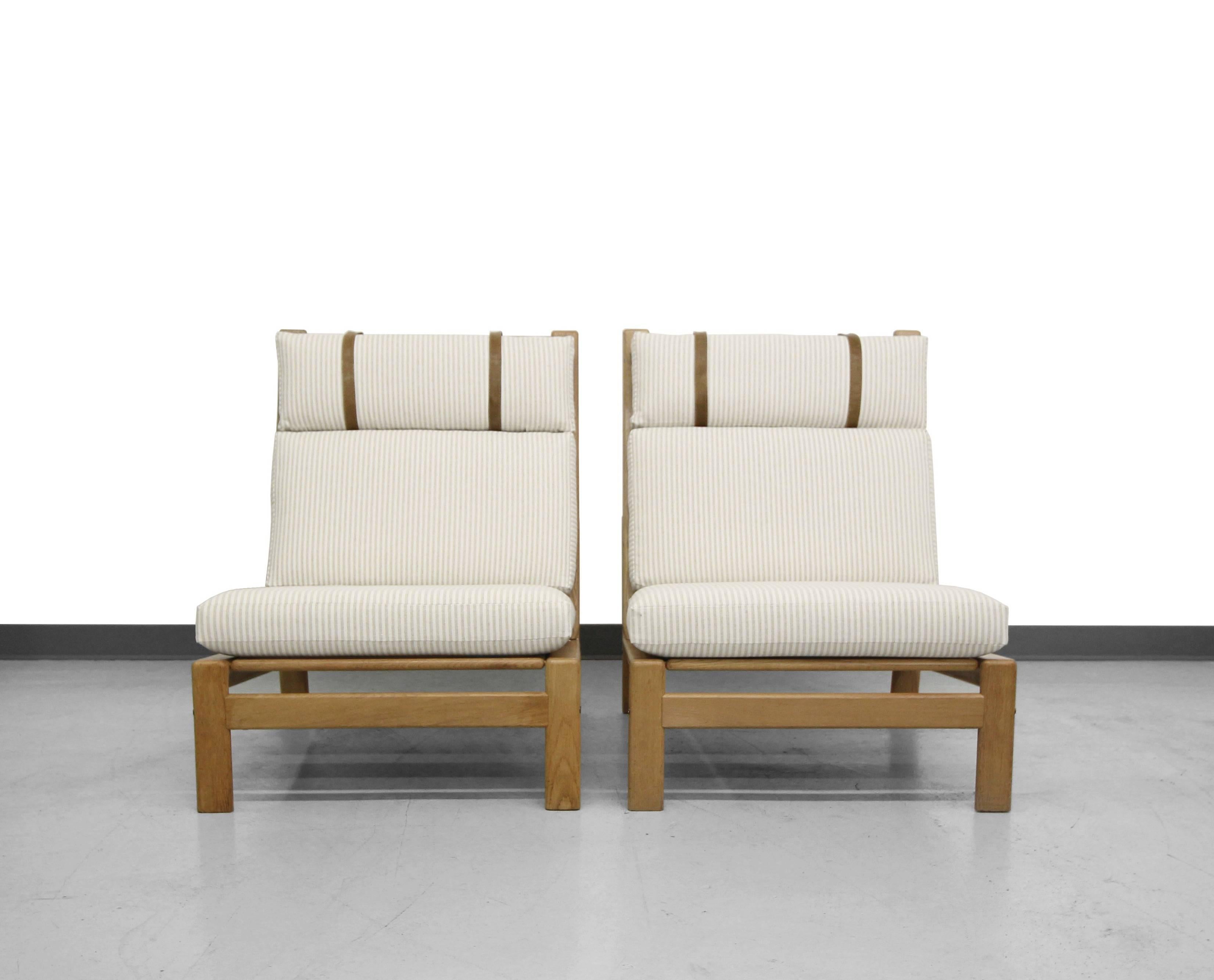 Rare solid oak framed Danish high back lounge chairs by Komfort design. Chairs are upholstered in a high quality seer sucker fabric with original leather straps.