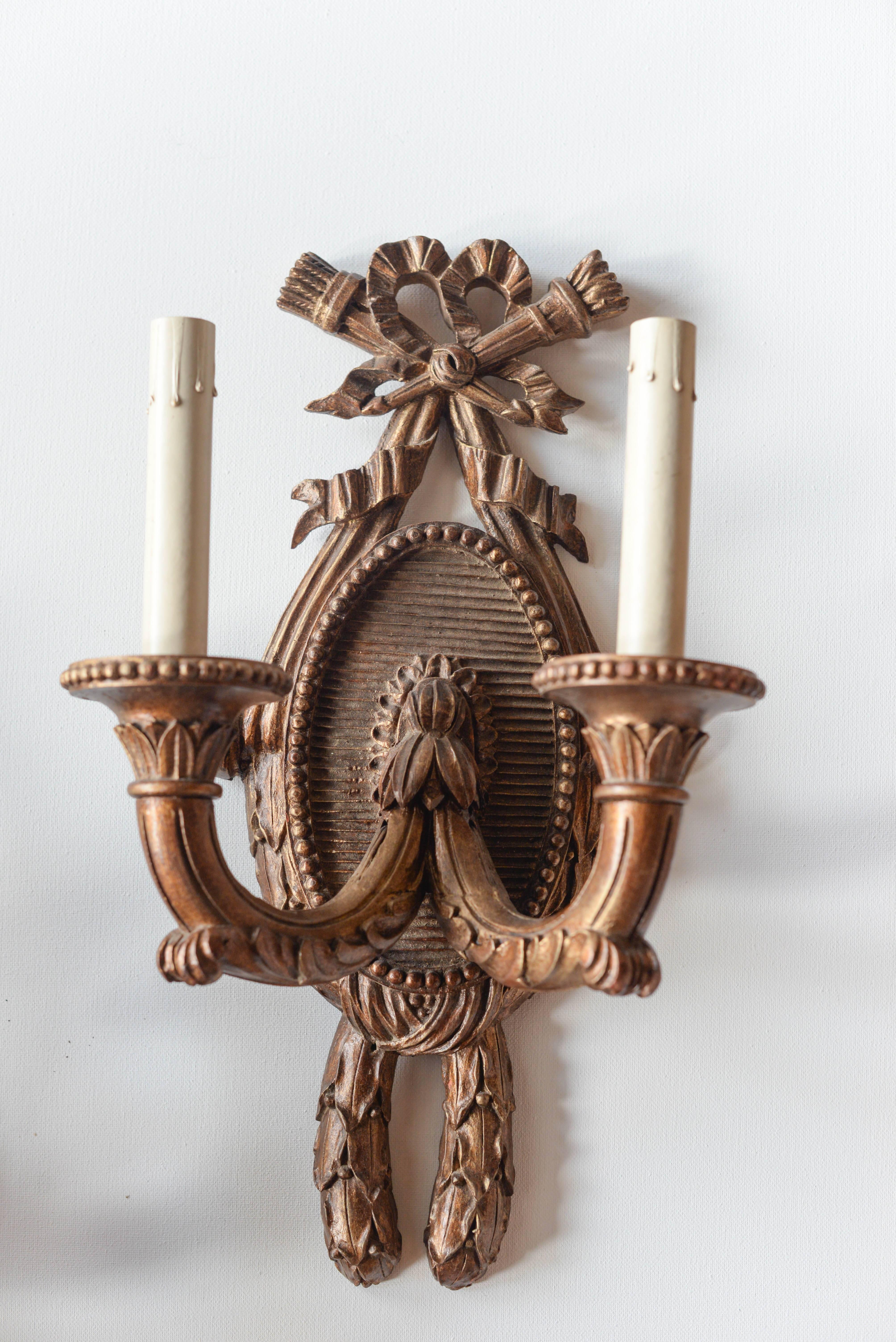 This pair of 19th Century French Carved Wood Sconces features on oval carved and beaded backplate with a lovely ribbon decoration.  The sconces have a gold / brown finish and have been newly rewired.