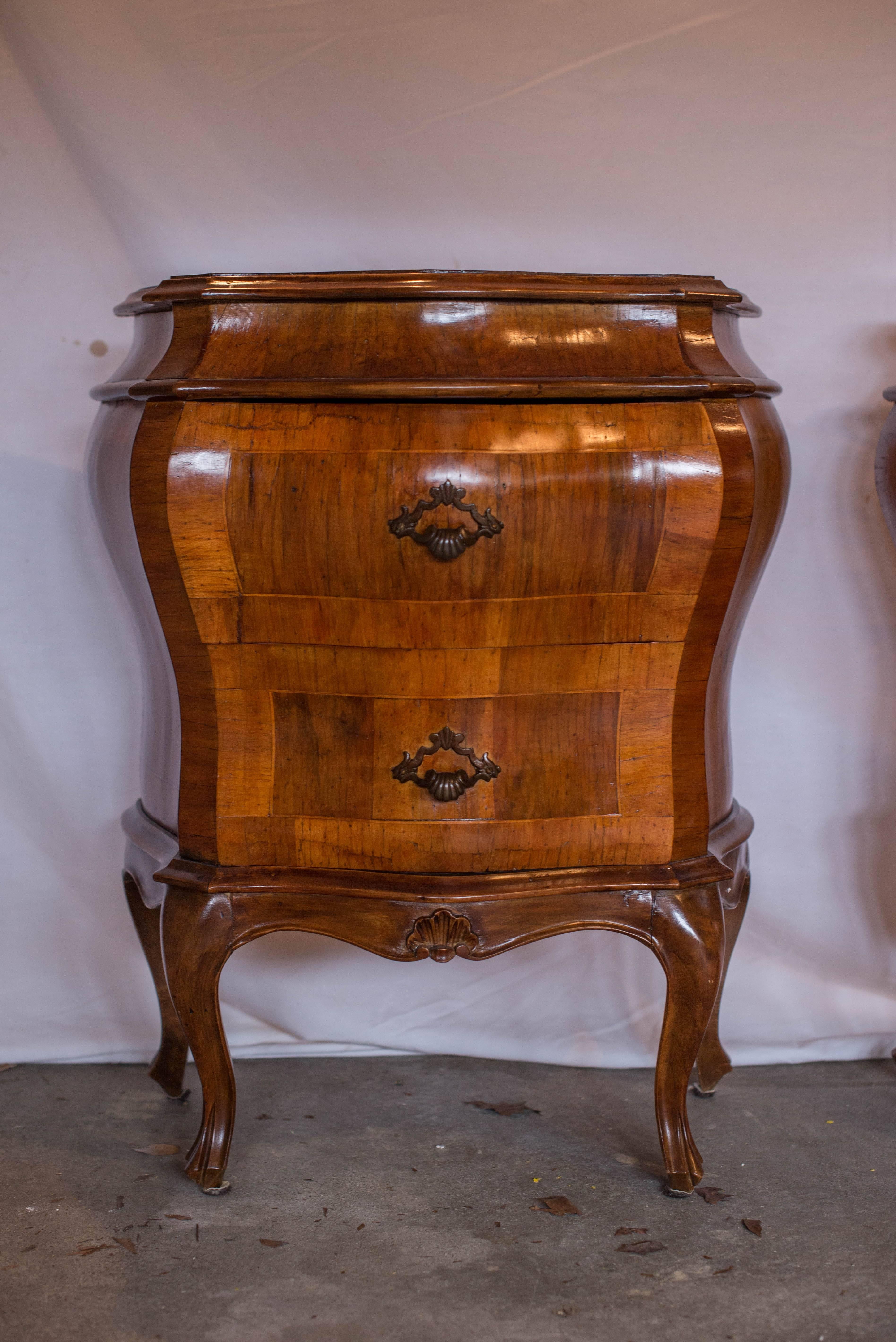 This pair of 20th century Italian Olive Wood Bombe two drawer commodes features beautiful inlay and a lovely shaped top.  The pulls are brass or bronze.