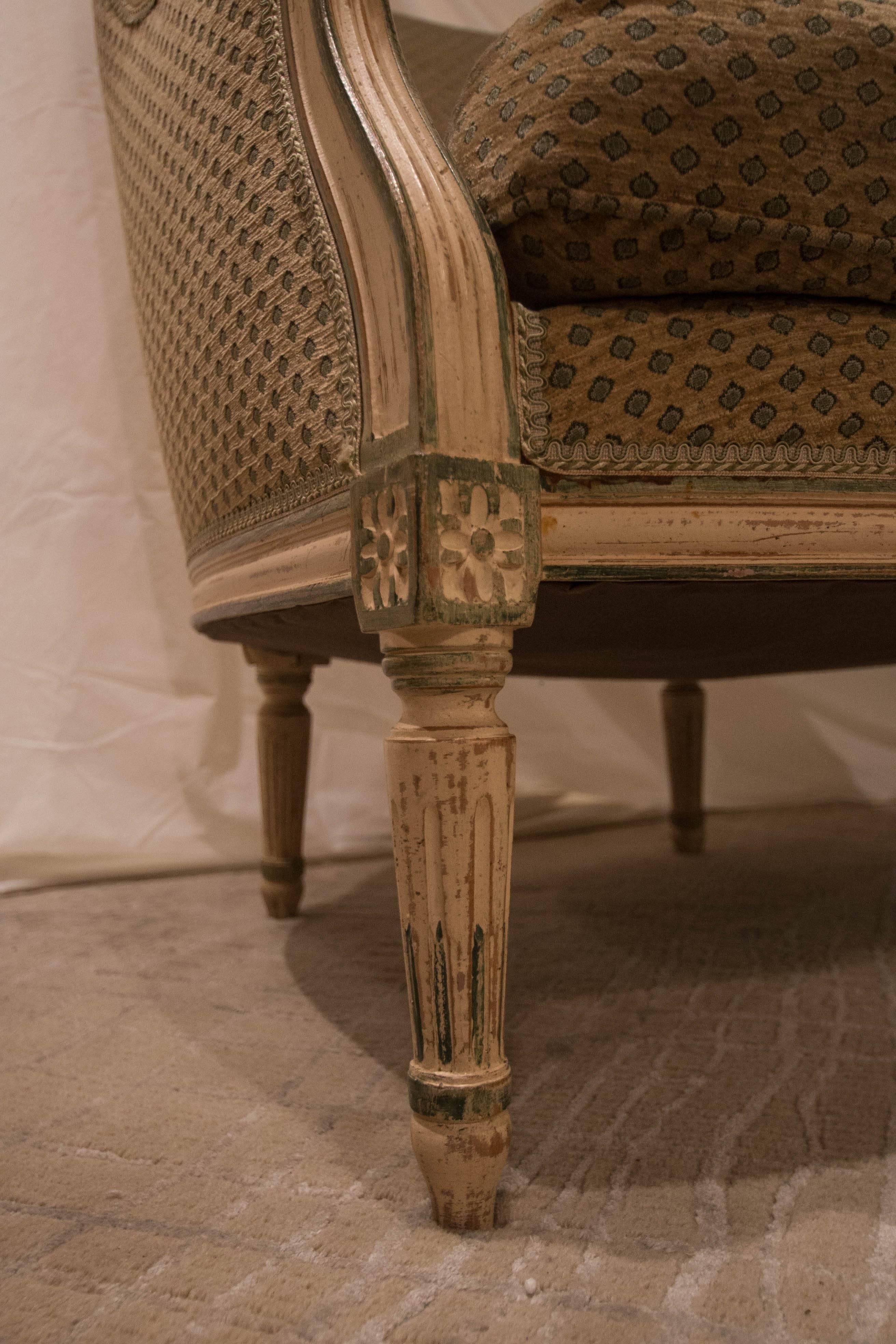 This pair of early 20th century French barrel backed Bergere chairs has a lovely painted finish that is creamy with green accents. The legs are fluted with rosettes and the upholstery is in good condition but not recently reupholstered.