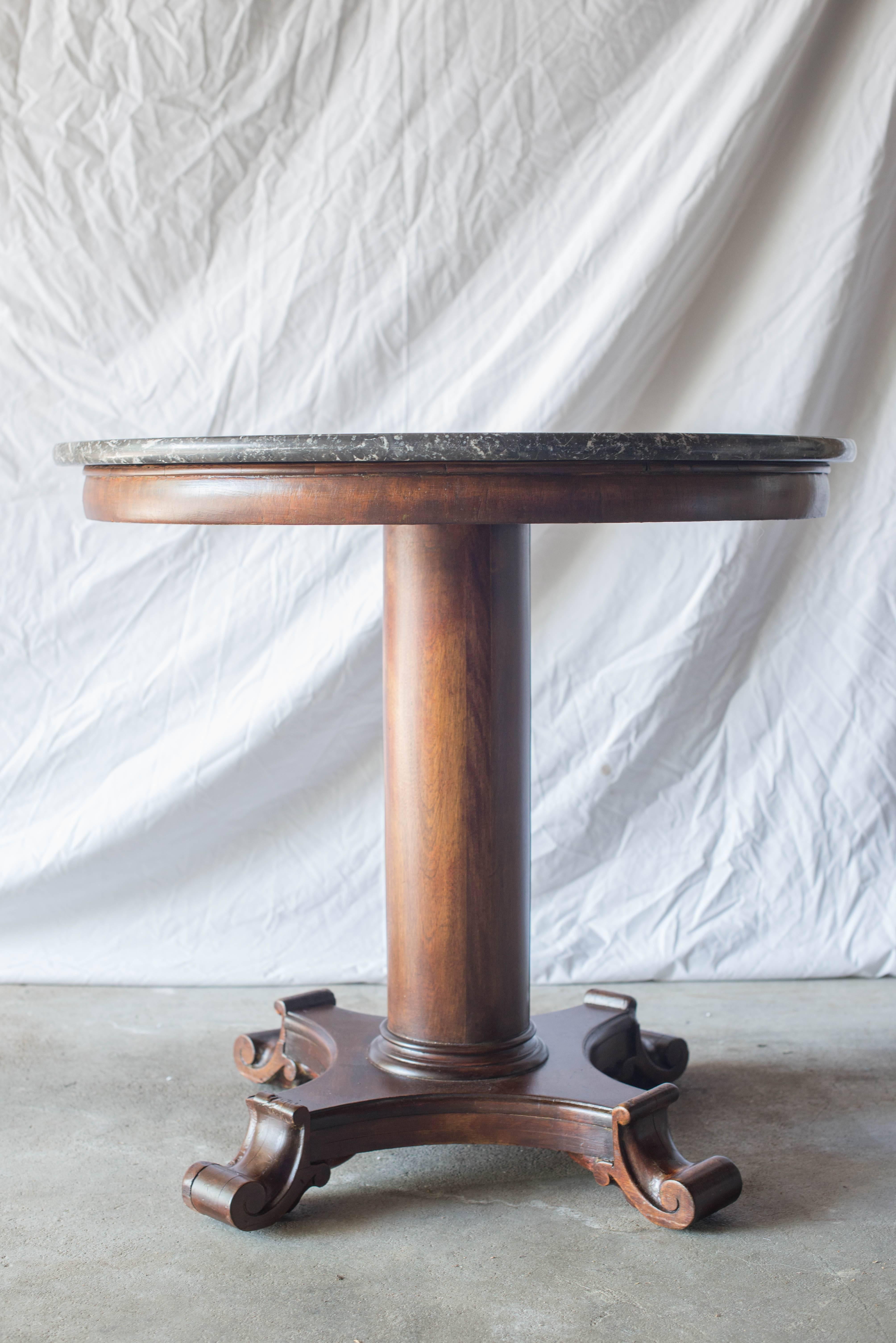 This table features a walnut pedestal base with unusual scrolling feet. The marble is a charcoal gray and is in excellent condition.