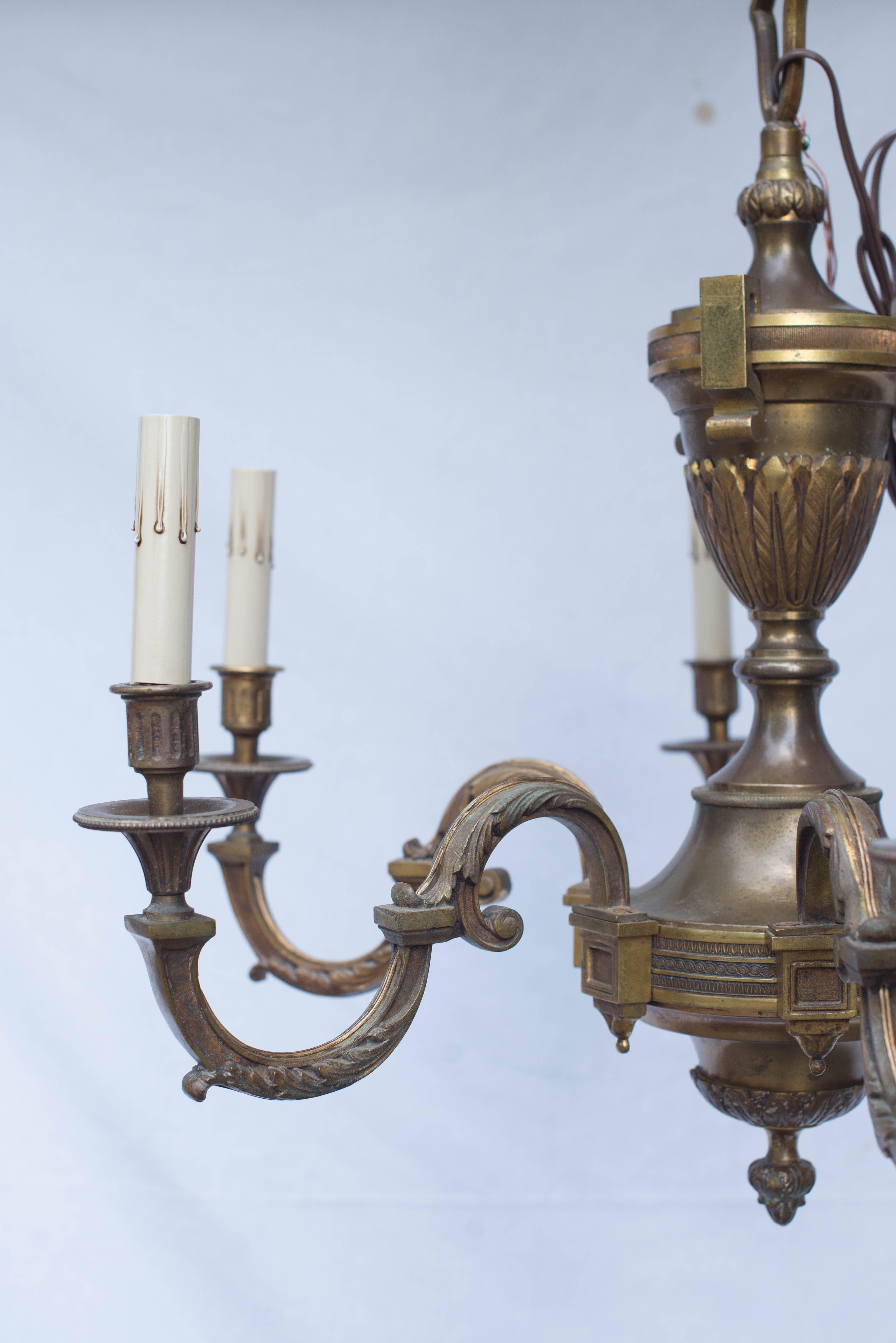 This early 20th century French Empire bronze chandelier has six scrolling arms with acanthus leaves radiating off of a central urn. This fixture has been newly rewired for American use.