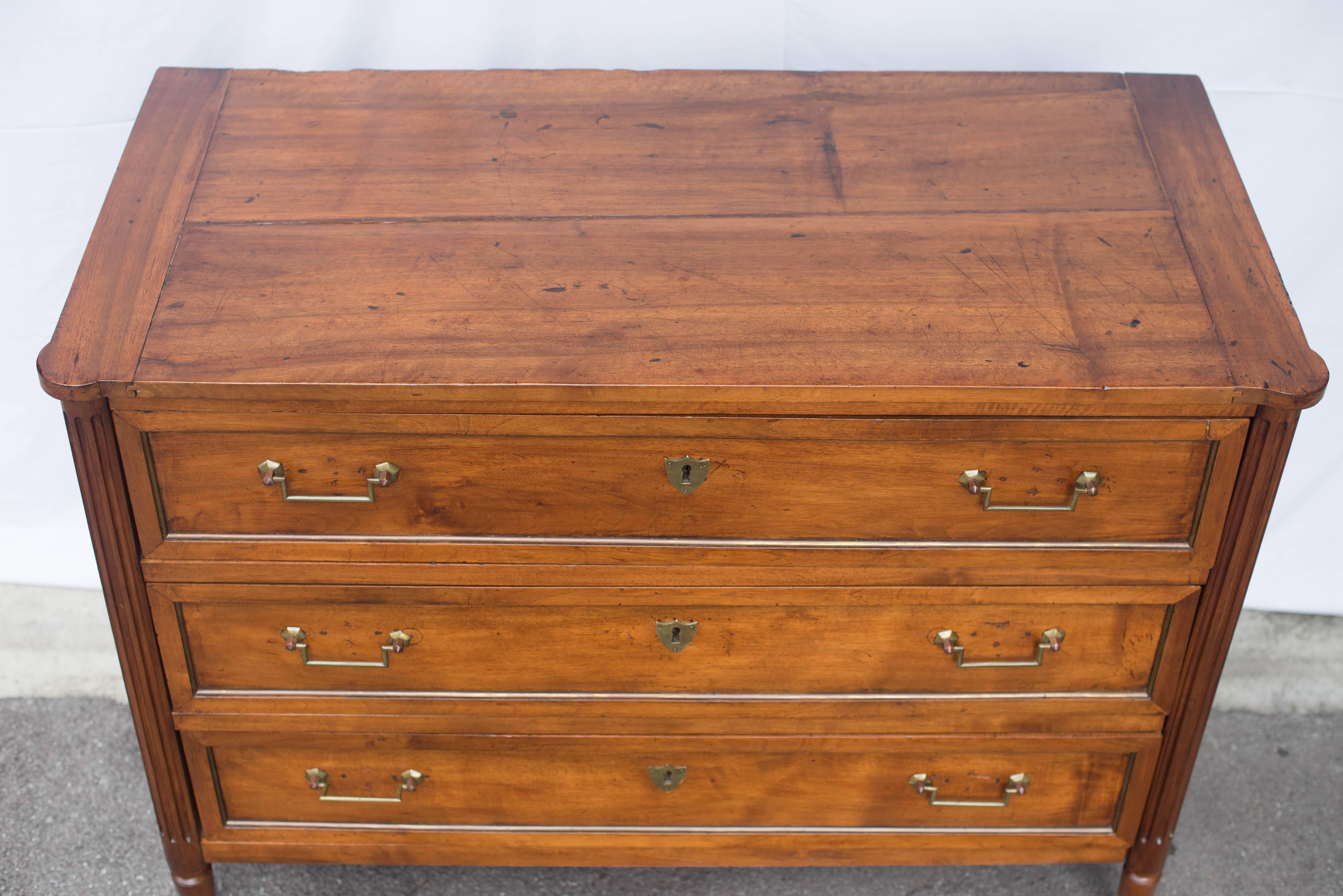This 19th century French walnut commode or chest of drawers features three drawers with Classic brass key escutcheons and drop handles. The legs are fluted and the sides paneled.