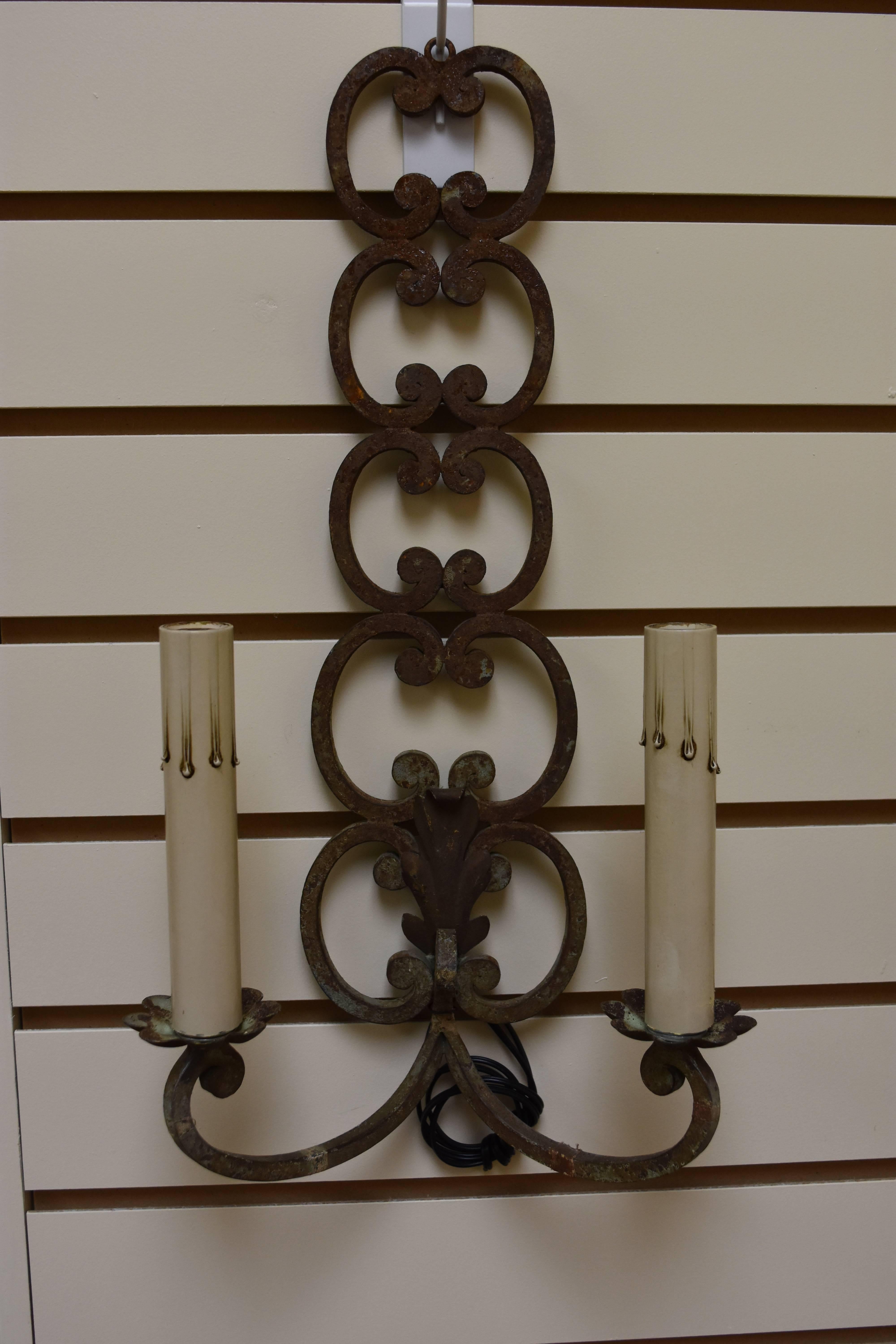 This pair of two-arm French iron sconces has been newly rewired for American use and boasts a unique scrolling design. The finish is a natural rusty / verdigris color.