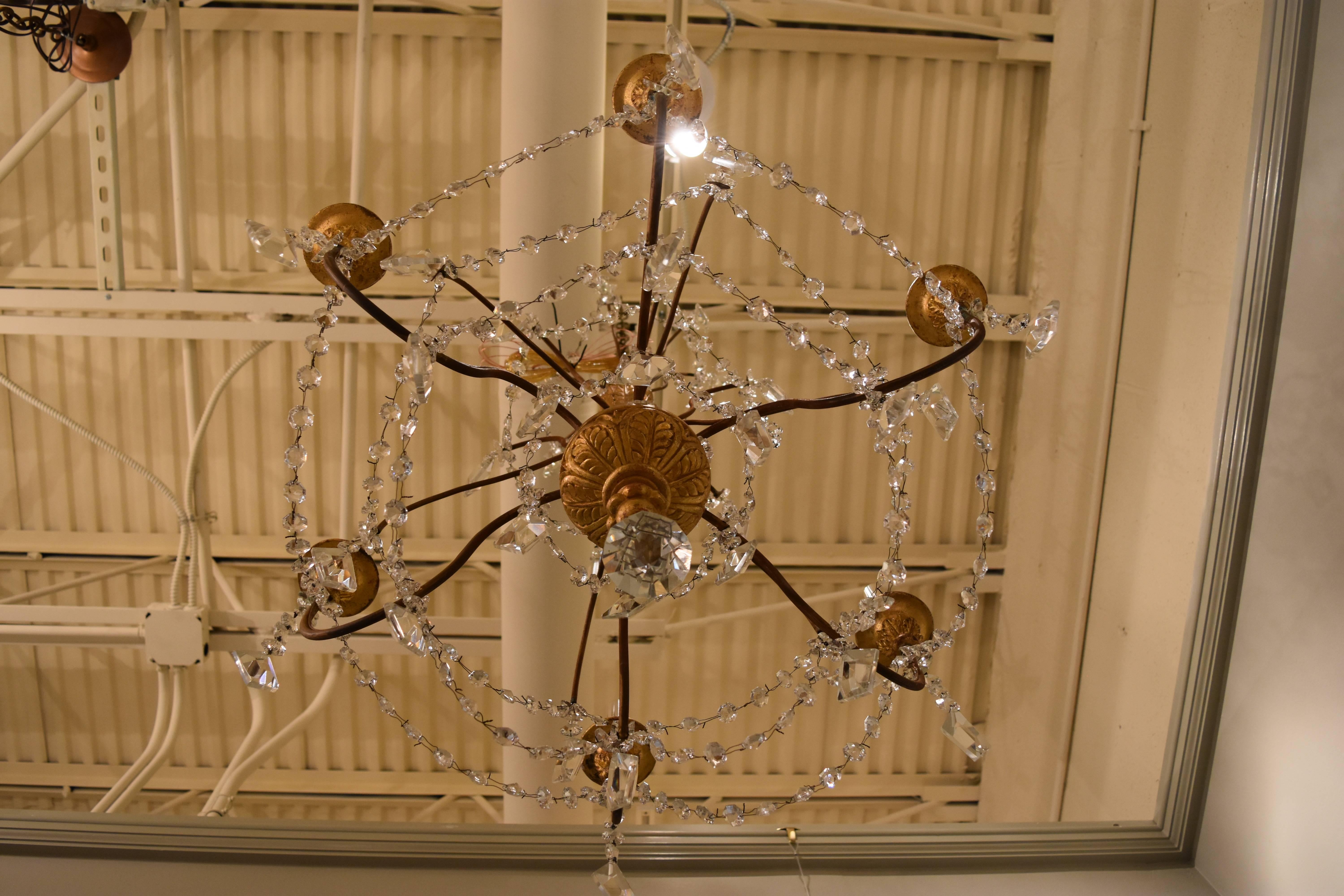 This 19th century Italian Genovese chandelier has six iron arms radiating off of a giltwood center. This piece has been newly rewired for American use. The crystal prisms are dainty and are pyramid like in shape.