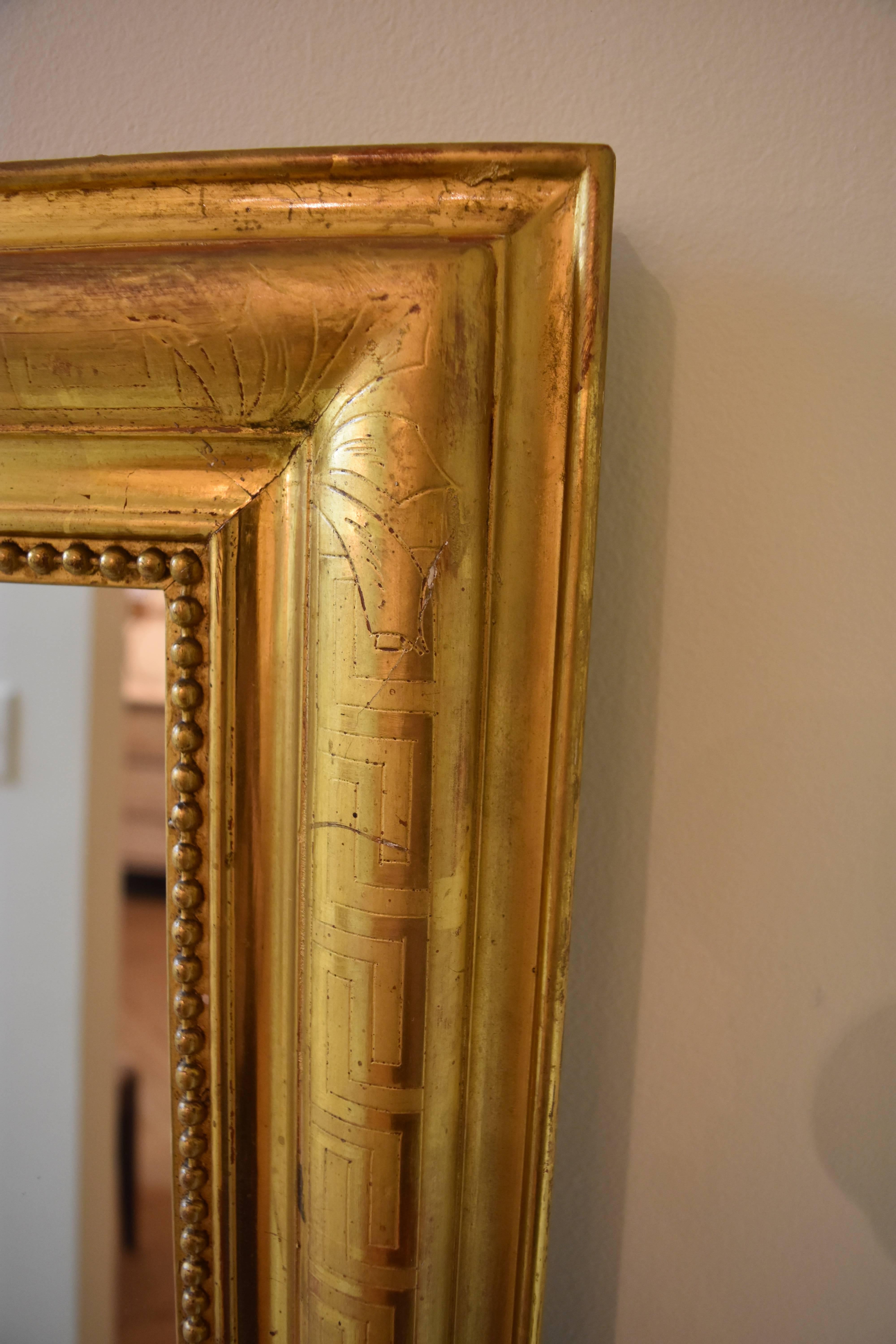 This large 19th century Louis Philippe giltwood mantel mirror features beading and a Greek key design.