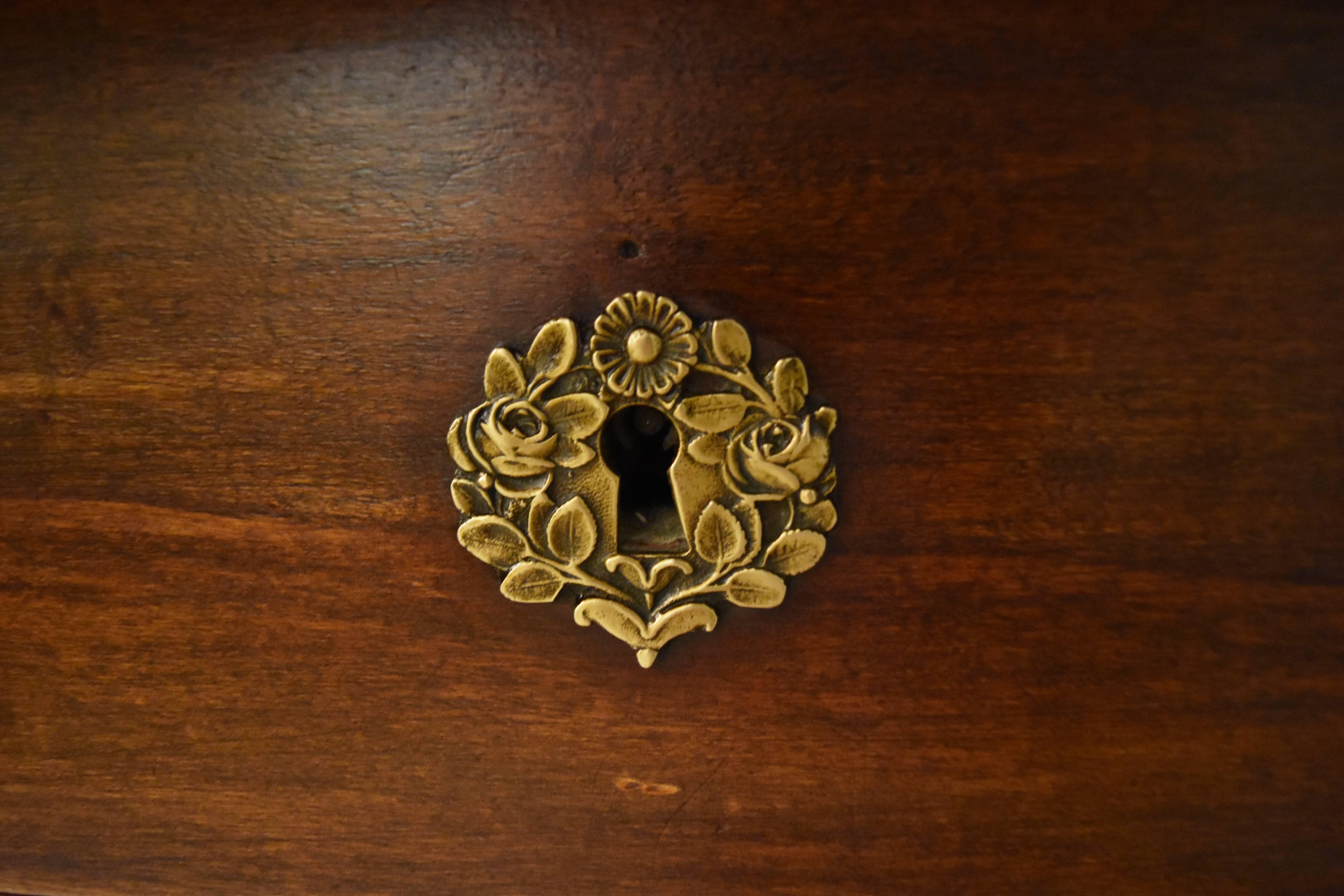 This exquisite French Empire Chest has three drawers with beautiful decorative floral brass pulls and key escutcheons and a top drawer with no pulls. The lower three drawers are flanked by columns with decorative brass capitals and bases. The size