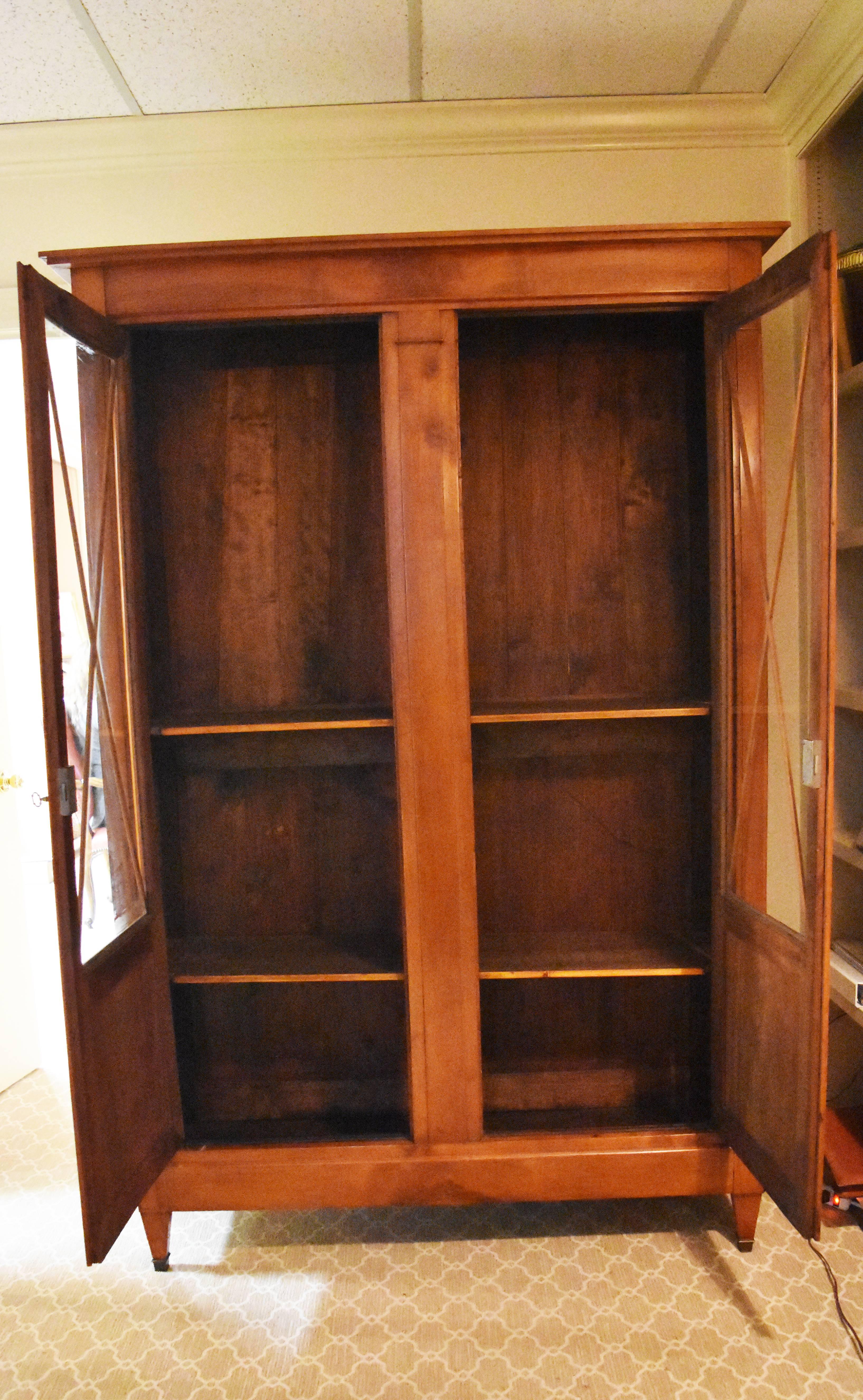 This 19th century Directoire style walnut bookcase features clean lines with two glass doors decorated with an 