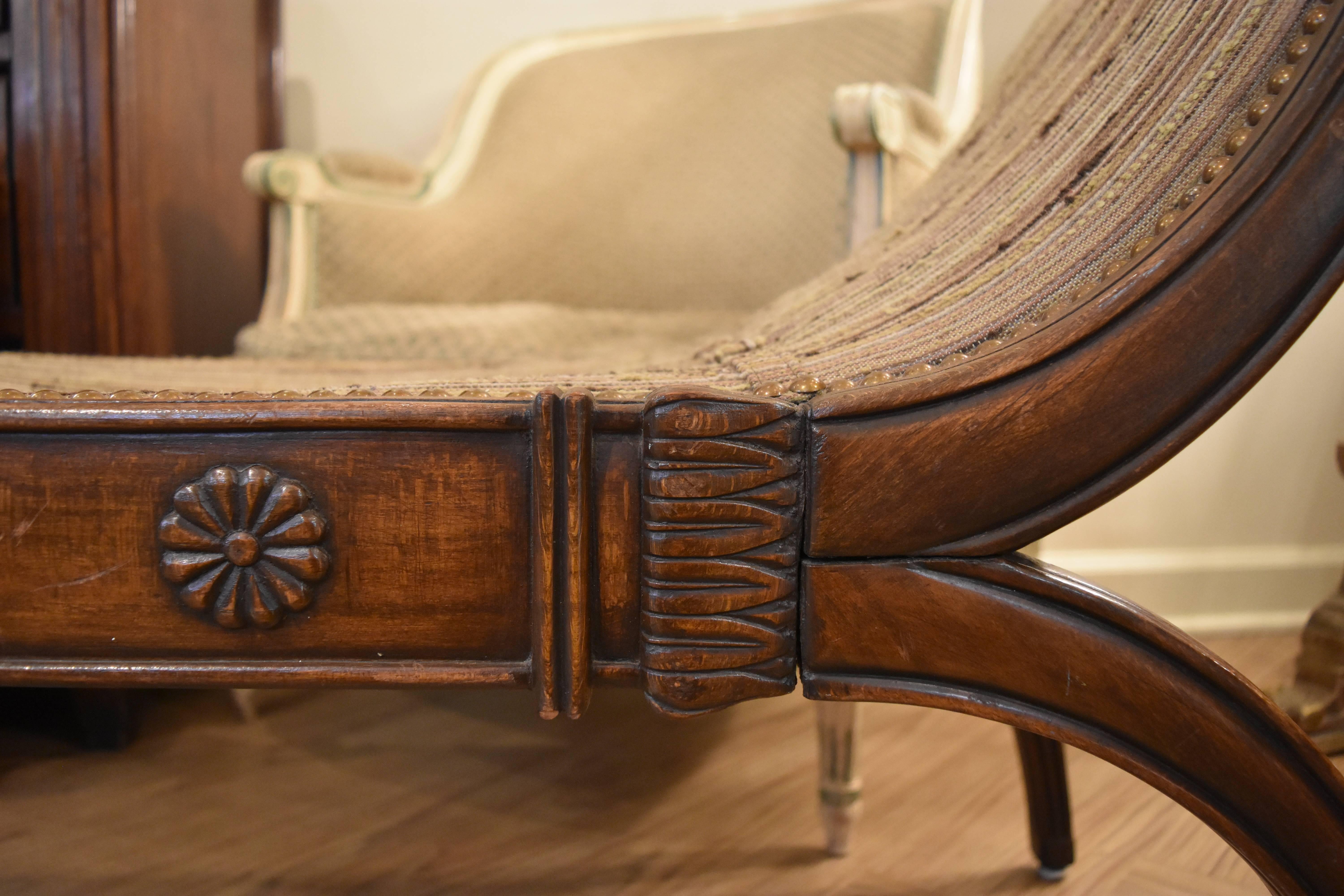 This hand-carved walnut French neoclassic or Empire style X-form bench features rolled arms and beautiful hand carvings.
It is substantial in size and would look fantastic with both traditional and transitional decor. The fabric is worn and needs