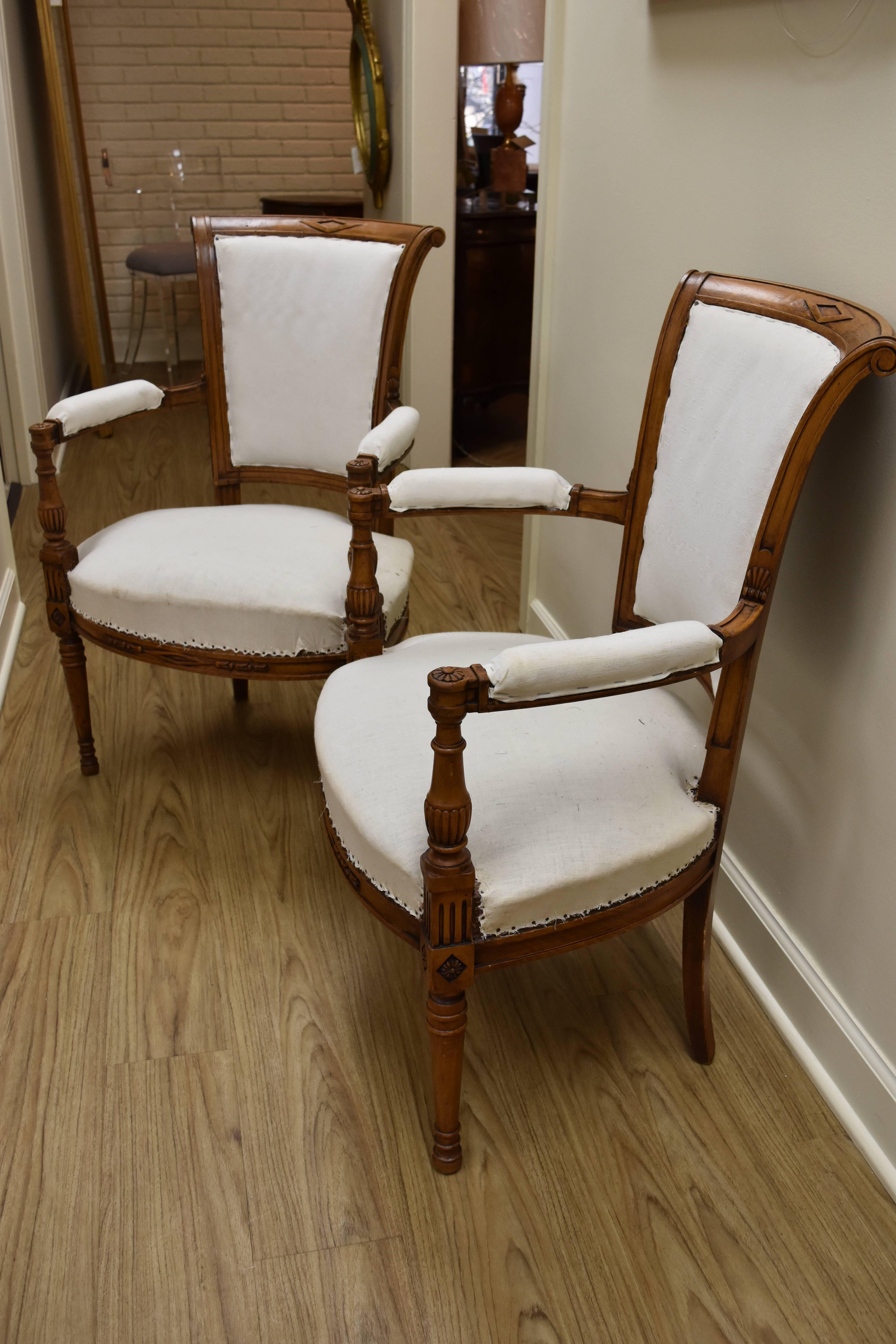 This pair of Directoire Style Armchairs feature a lovely warm walnut finish with a scrolling back.  The fabric shown is a white duck cotton so the chairs will need to be upholstered.  The chair frames, arms and legs have hand carving with rosettes