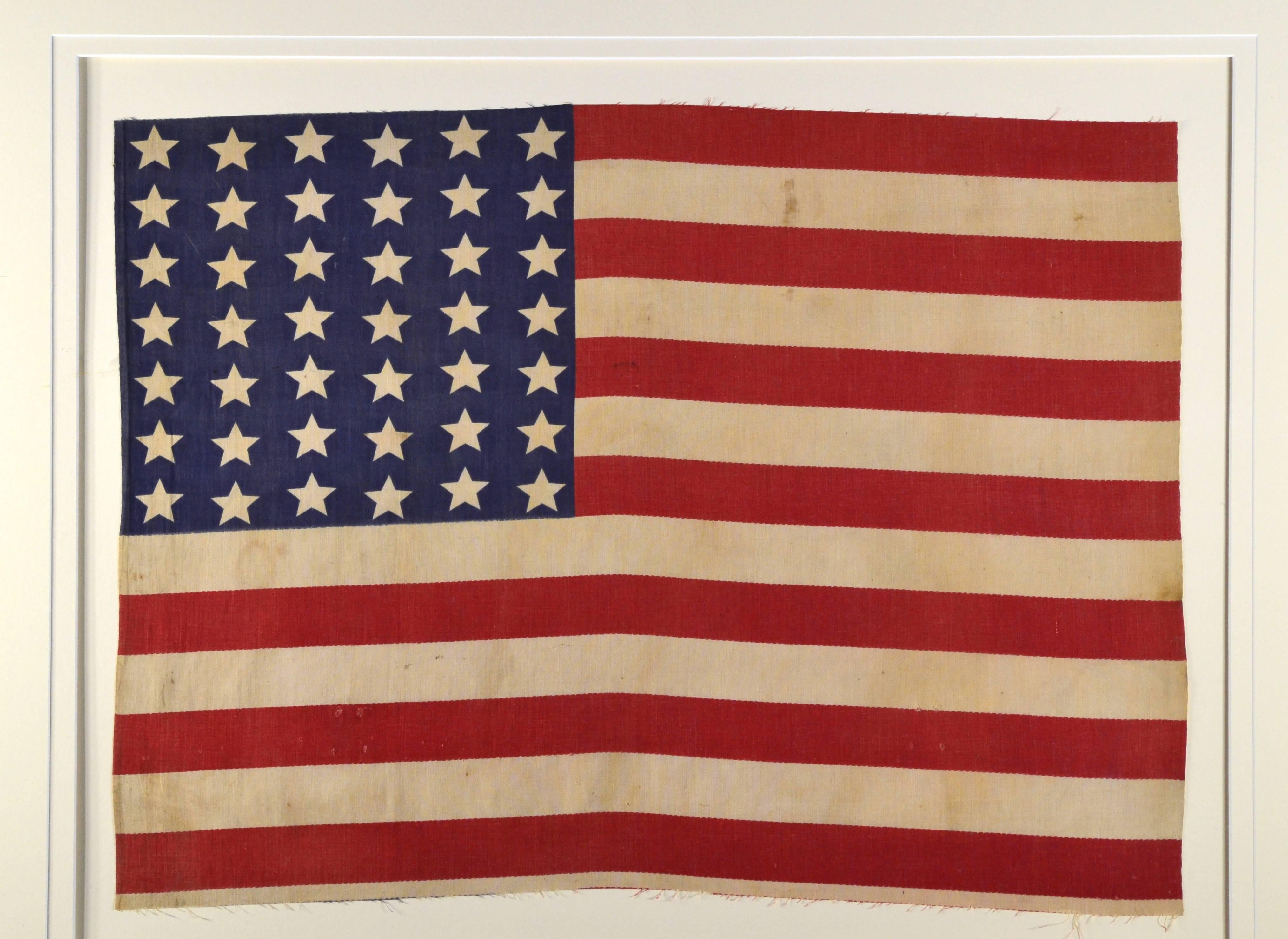 Antique 42 star American flag with conservation framing with UV acrylic. Made of cotton and would have been attached to a stick. The flag measures 18