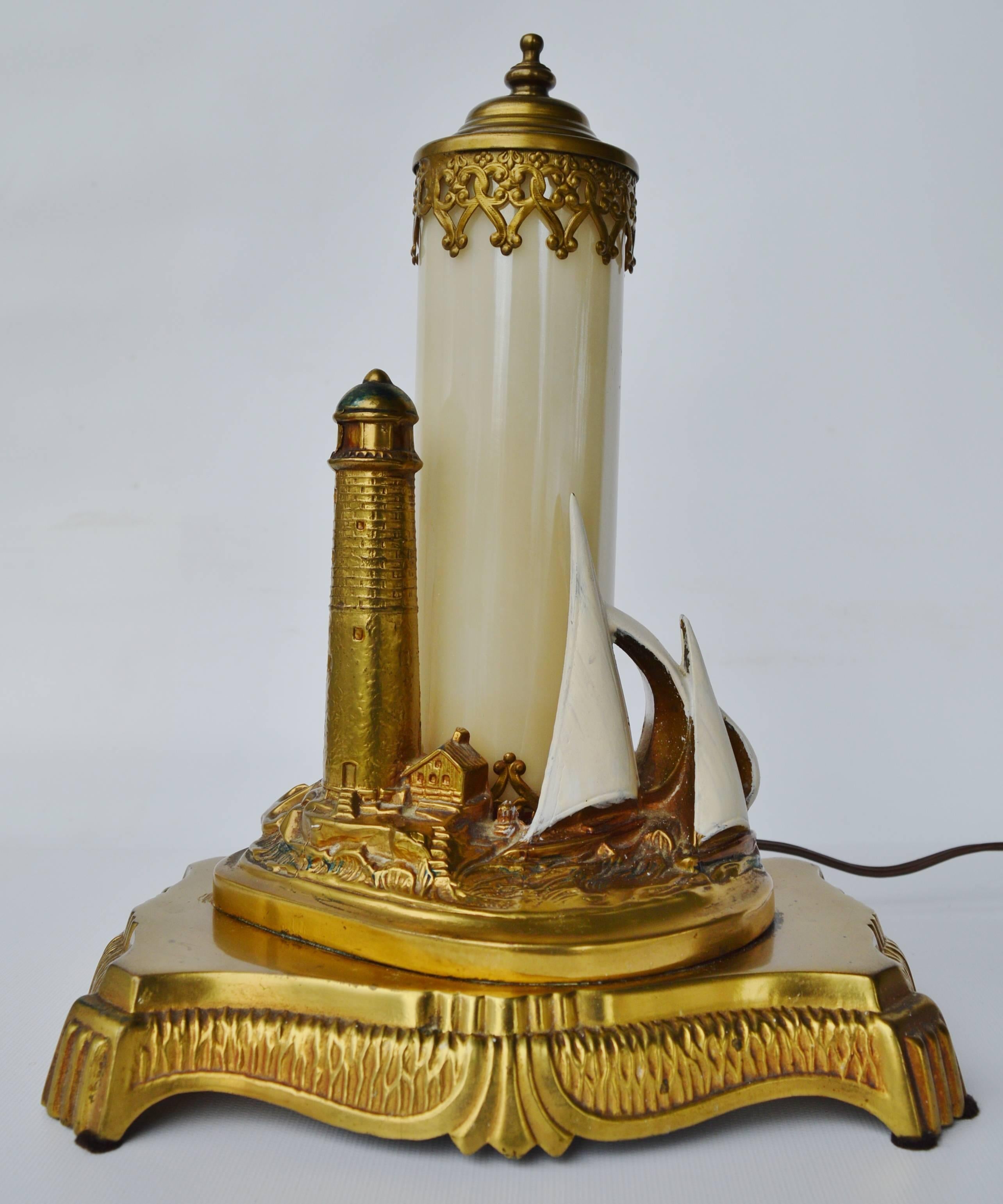 This amazing antique brass Art Deco table lamp is so detailed! Featuring a scene of a rocky shore line with light house, an out building, sailboats, crashing waves, and an anchor, with a pearl colored opalescent glass cylinder light with detailed