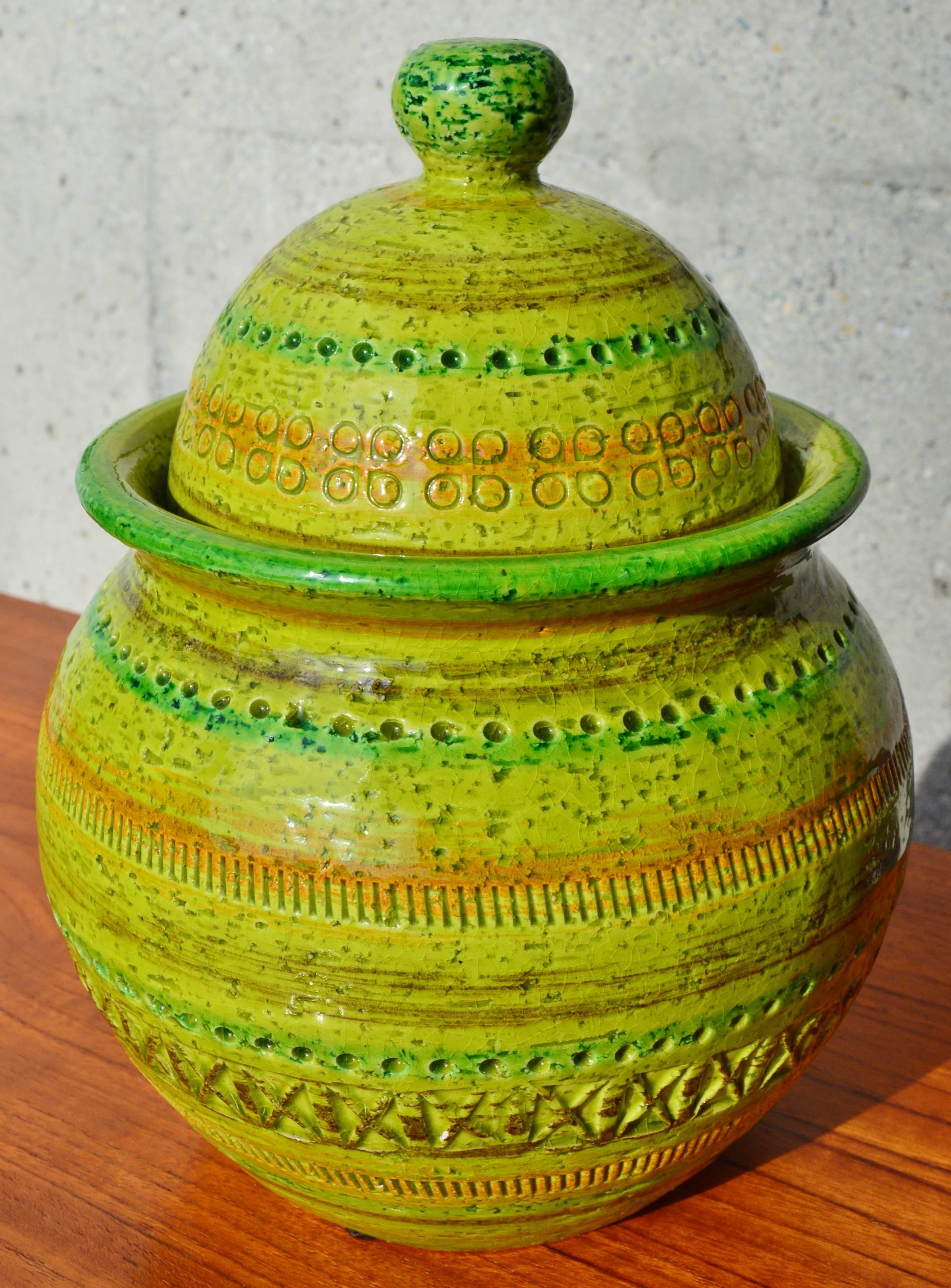 This stellar Bitossi ceramic lidded jar is in awesome shades of green with a touch of orange. The squat base is echoed by the shape of the lid. Striking piece for a pop in your decor. The only flaw is a small chip on the lid base where it is