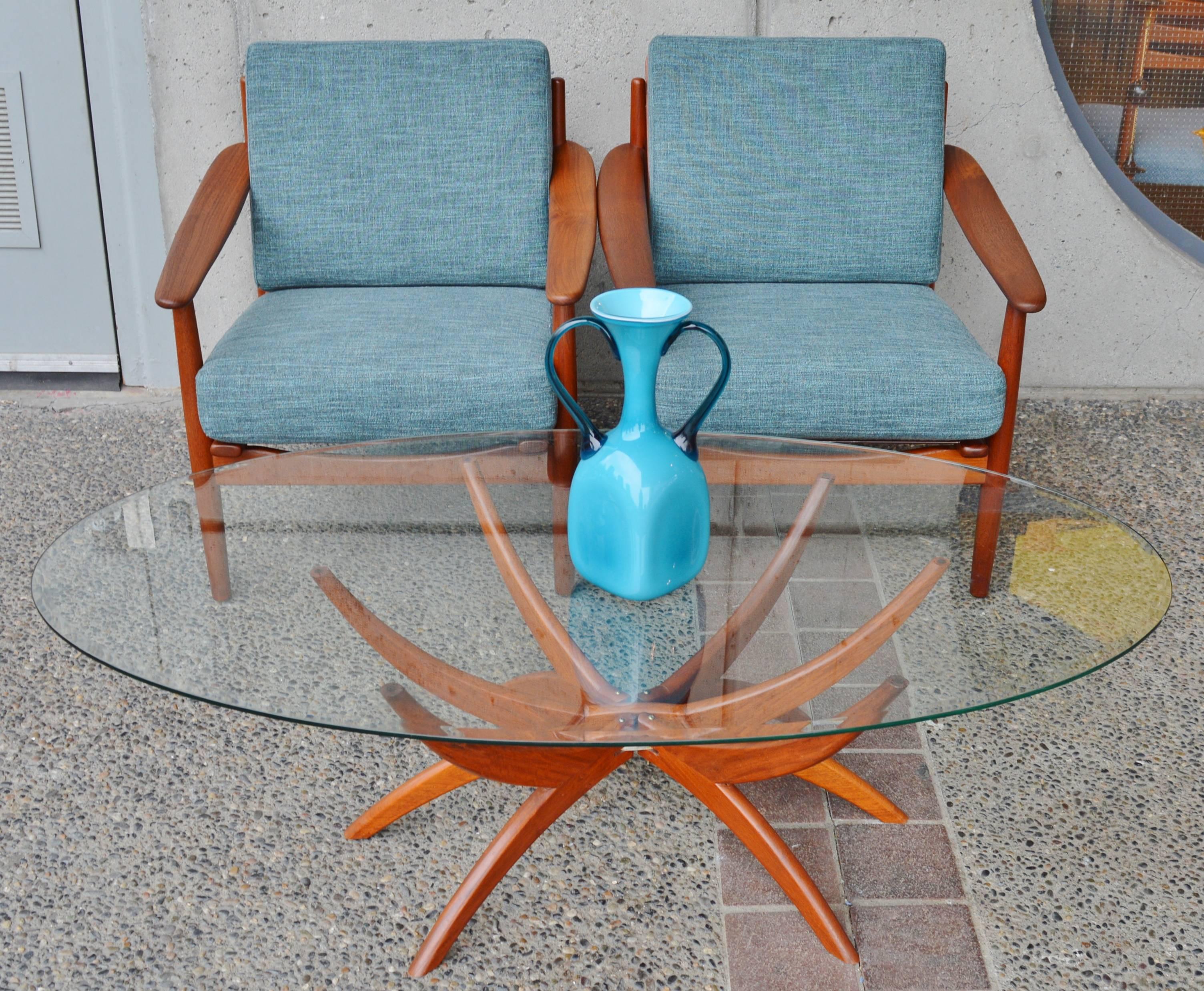 This totally killer Danish modern teak spider leg coffee table is much in the style of those made famous by Vladimir Kagan. Featuring beautifully contoured double curved legs that fold flat for easy transport, with an oval beveled edge glass top.