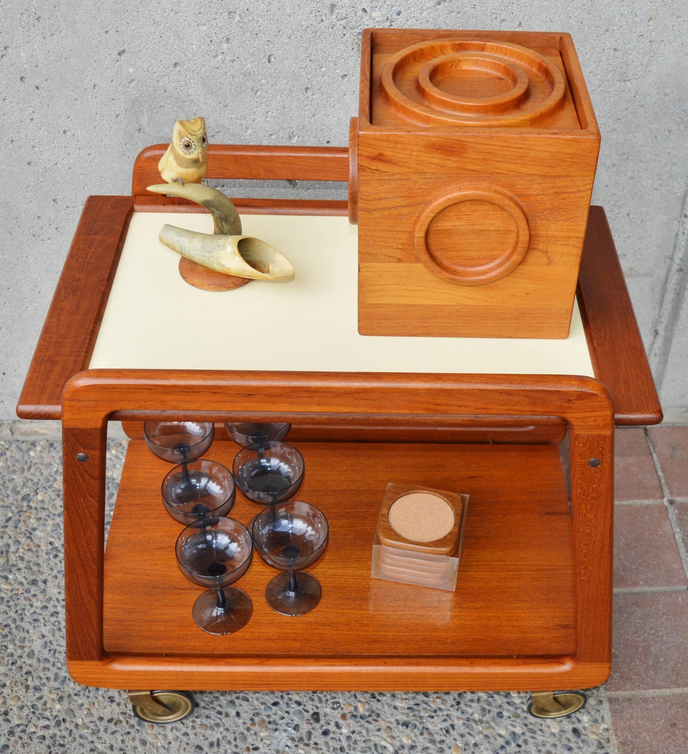 This is a super fun Danish Modern teak cart with unlimited useful purposes! Featuring solid teak trapezoidal shaped sides, a lower shelf floating on brass pins, Classic skinny 1950s brass casters and a flip-top tray that is teak on one side or pale