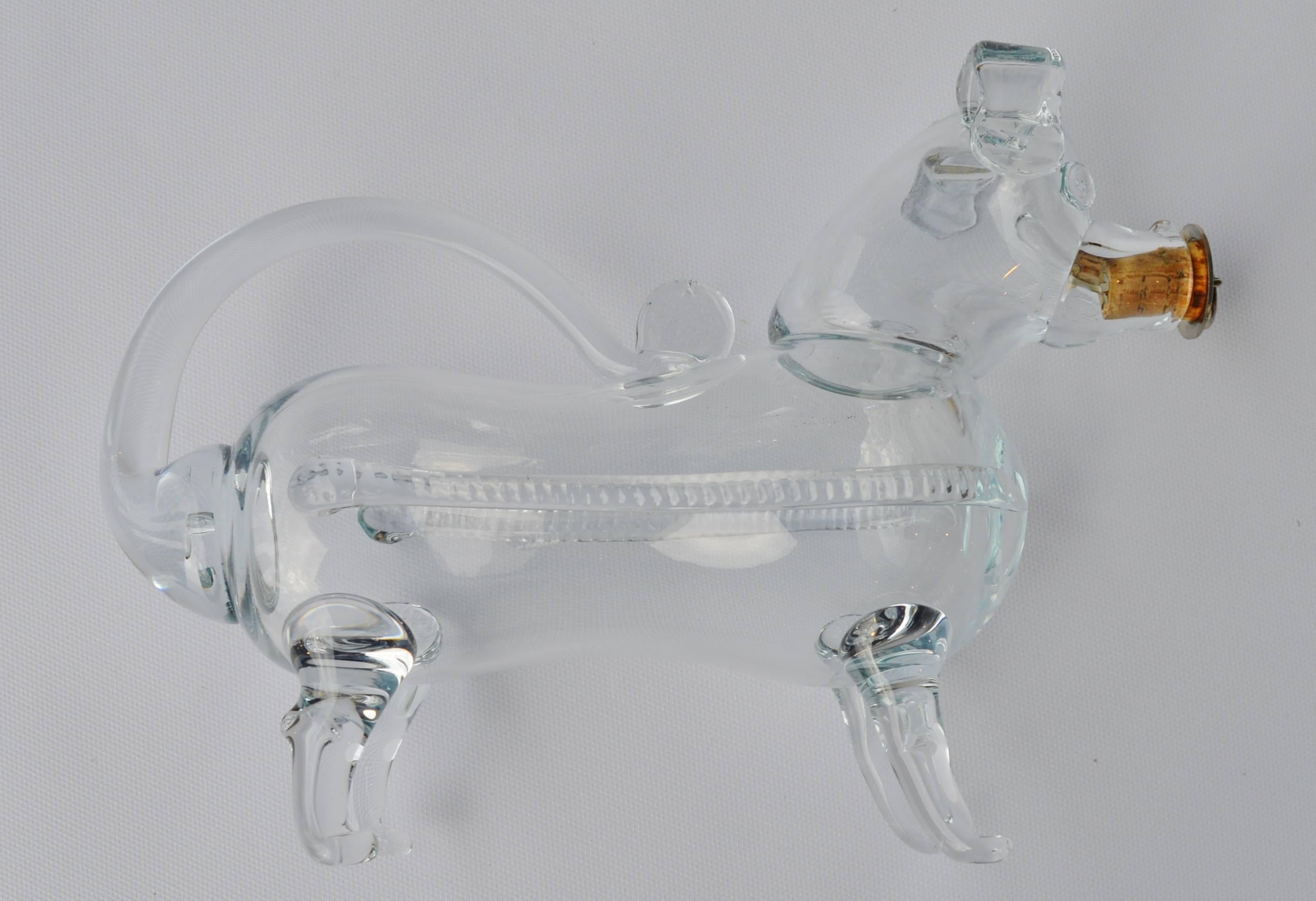 A whimsical dog-form decanter handblown in clear glass with the cork in his snout and the tail forming the carrying handle. This type of decanter is also referred to also as a gin pig, and was made by Holmegaard Glassworks and is in excellent