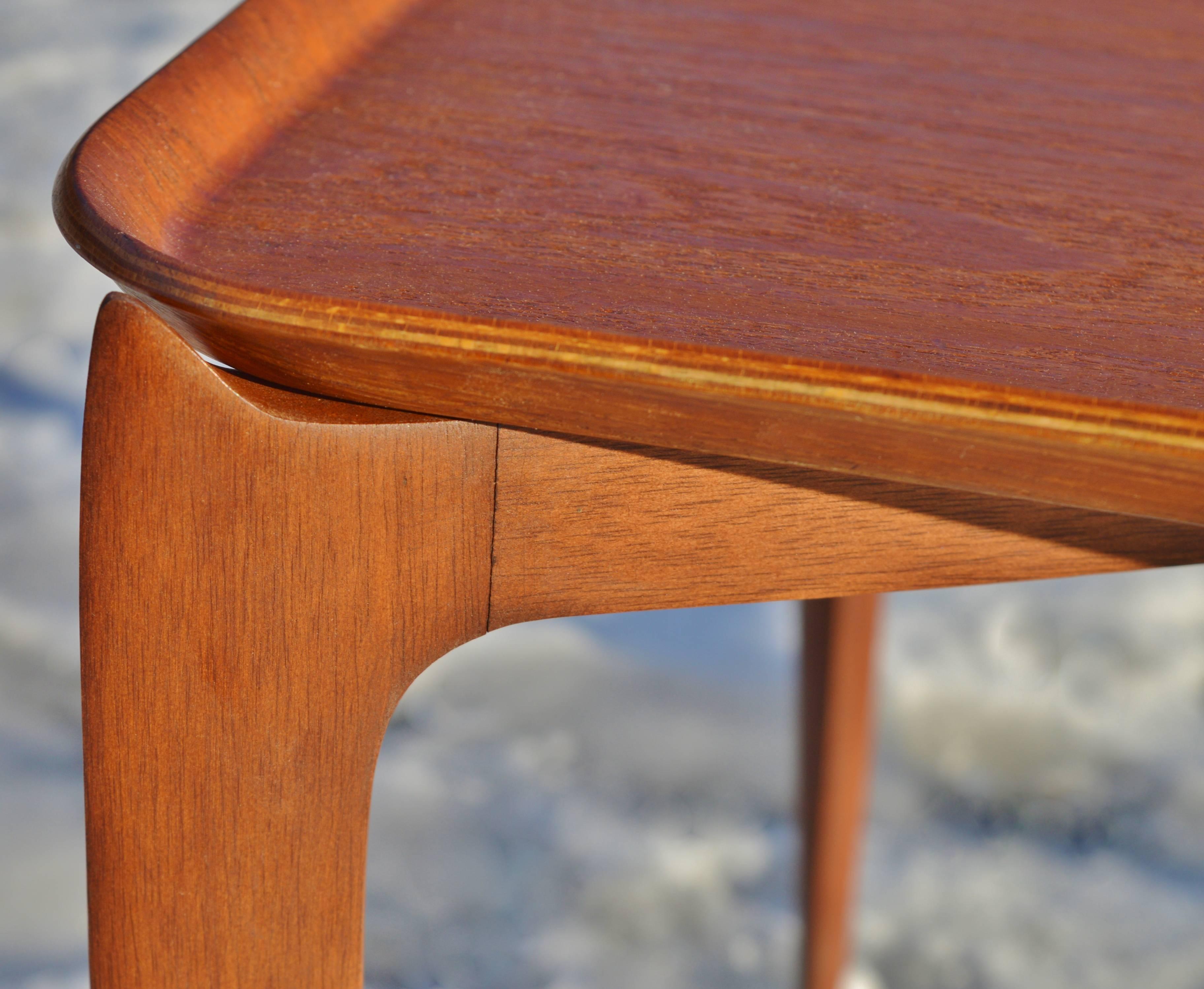 An elegant rectangular teak tray table was designed in the 1950s by Svend Åge Willumsen and H. Engholm for Fritz Hansen. This is the rare rectangular version with the spider leg folding base that flares at the top to nestle around the curves of the