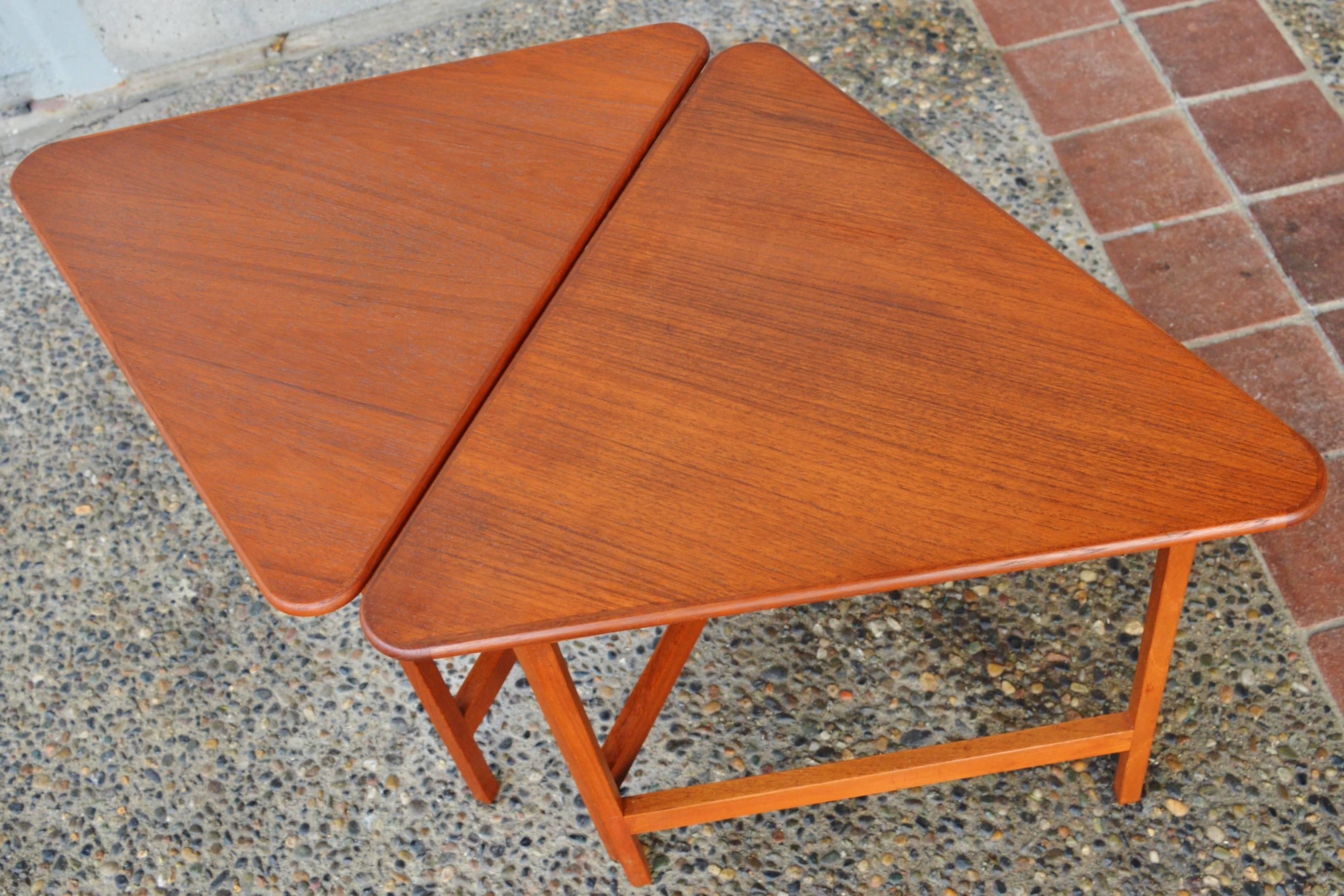 This totally fun pair of restored Danish modern teak folding tables are a clever design by Illum Wikkelsø. The tops are rounded triangles, and the legs fold out like a gate leg table with brass hinges, and a ball catch and stopper to hold them in