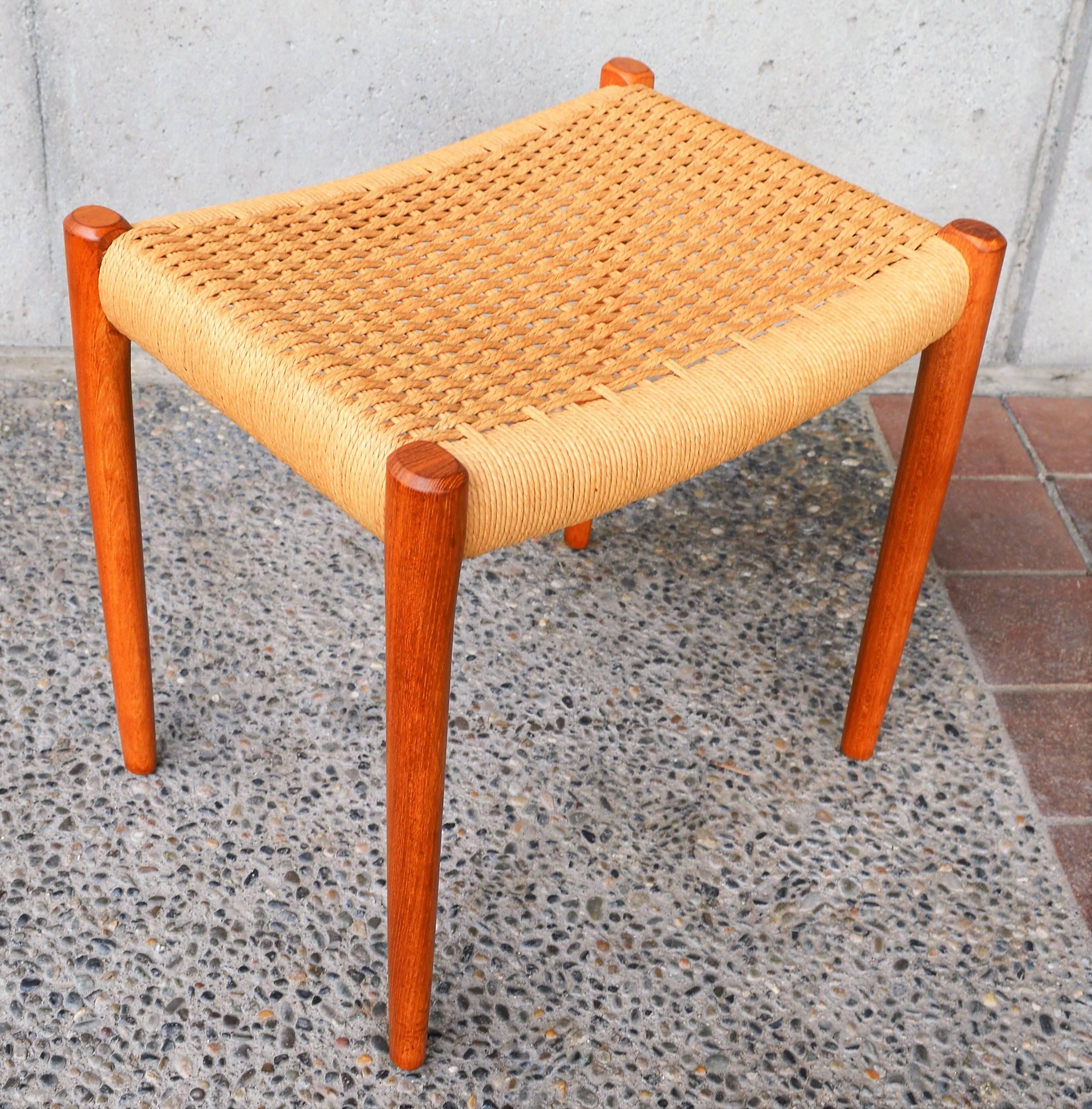 This lovely Danish modern teak stool or ottoman by Niels Otto Møller for J.L. Moller is in absolutely amazing original condition. With solid teak sculptured and tapering legs with beautiful grain, and the original basket weave Classic Danish