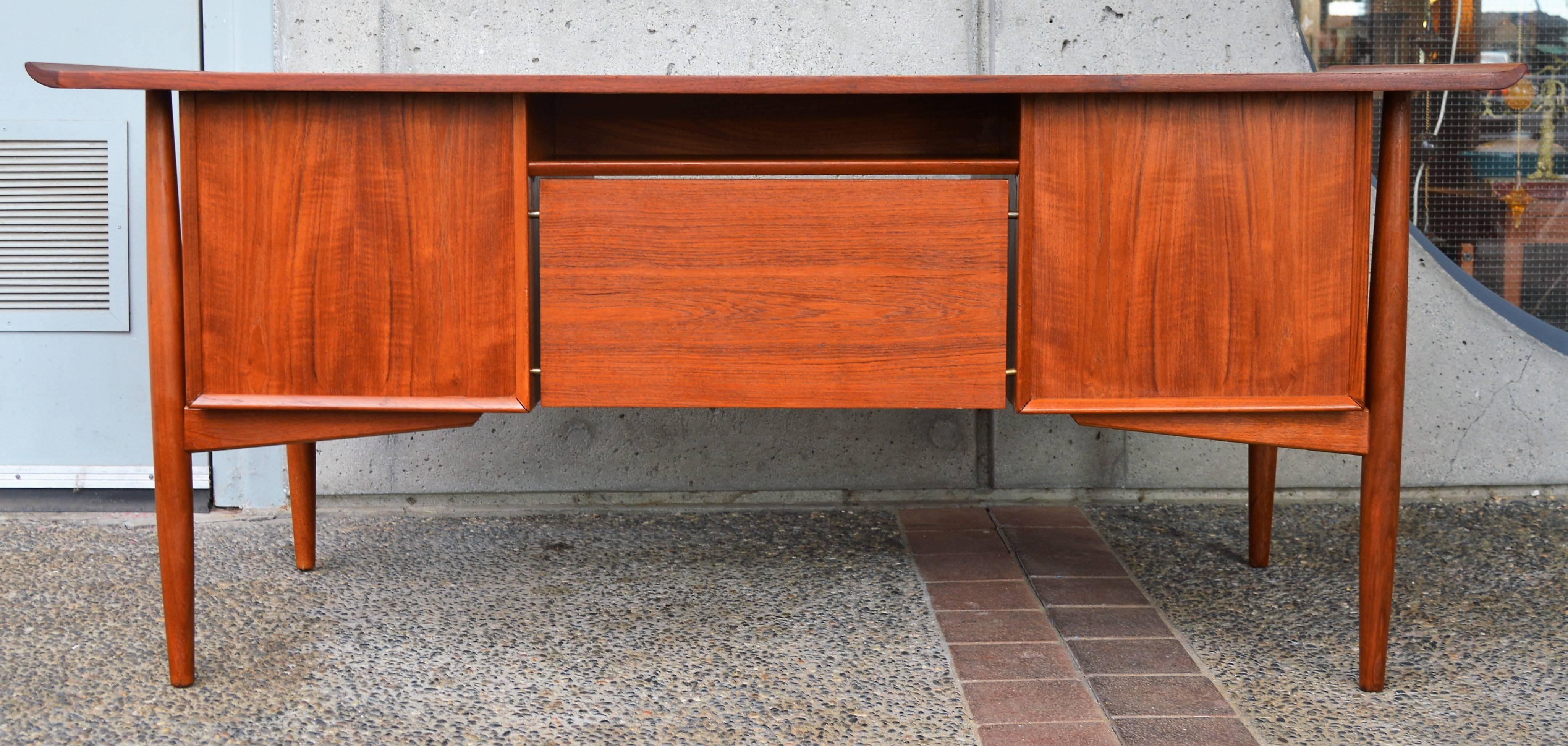 This stellar Danish modern quality teak desk was designed by Arne Vodder for H.P. Hansen in the 1960s. Note the beautifully flared ends on the top of the desk, the floating leg braces, the elongated drawer pulls, the floating back board on brass
