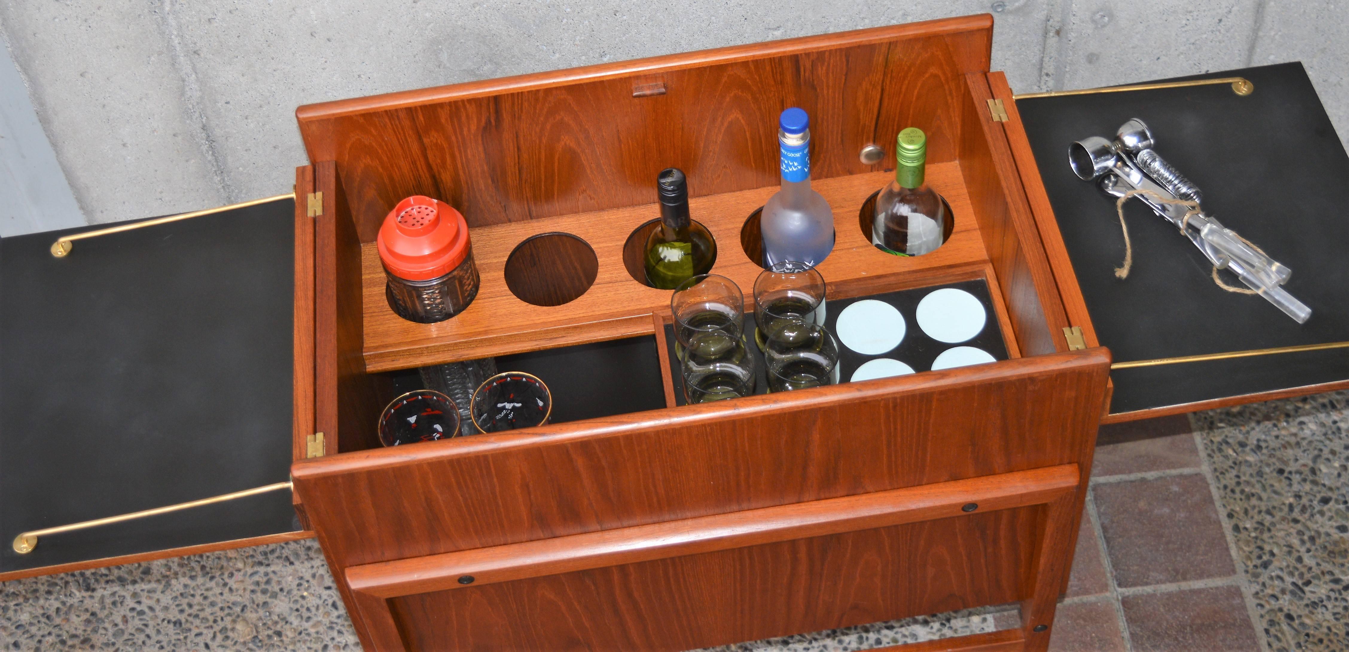 This lovely quality Danish modern teak bar cabinet / cart gives you so much more bang for your buck than the standard two tier bar cart, as it can house a pretty significant home bar. Opening the two top doors and dropping them down, exposes black