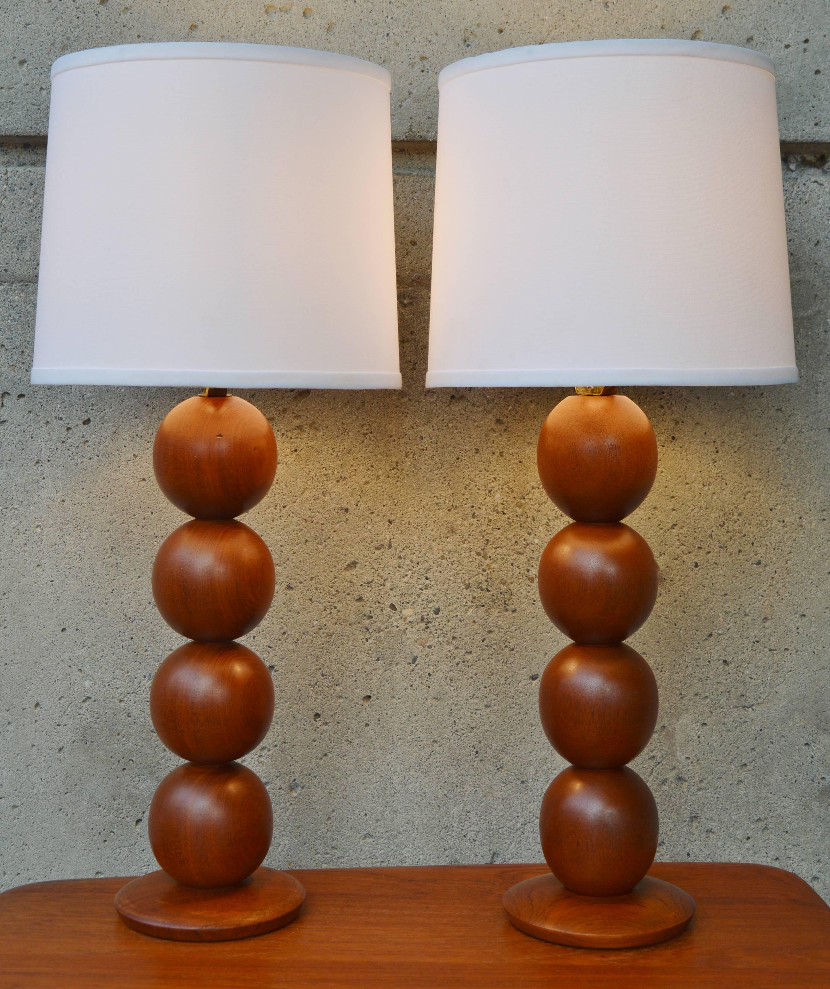 This wonderful geometric pair of Danish modern teak lamps are super dramatic, without taking up too large of a foot print. Featuring a contoured teak base and four teak stacked balls. Finished with new linen barrel shades in white. In wonderful