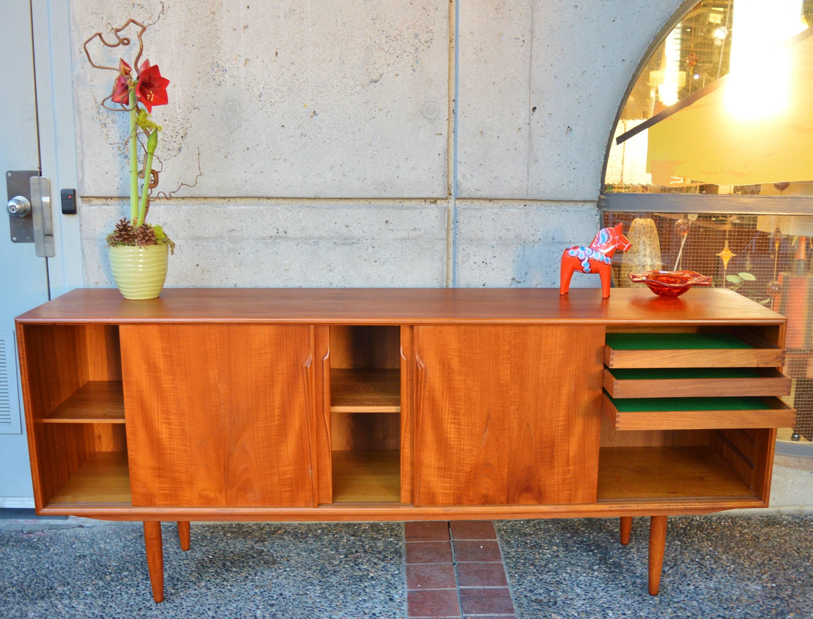 This stunning Danish Modern teak credenza or buffet was designed by Gunni Oman for Axel Christensen in the 1960s. I adore the two different sets of intricately carved door pulls! Featuring a lovely wood tone, with book marked veneers on the doors.