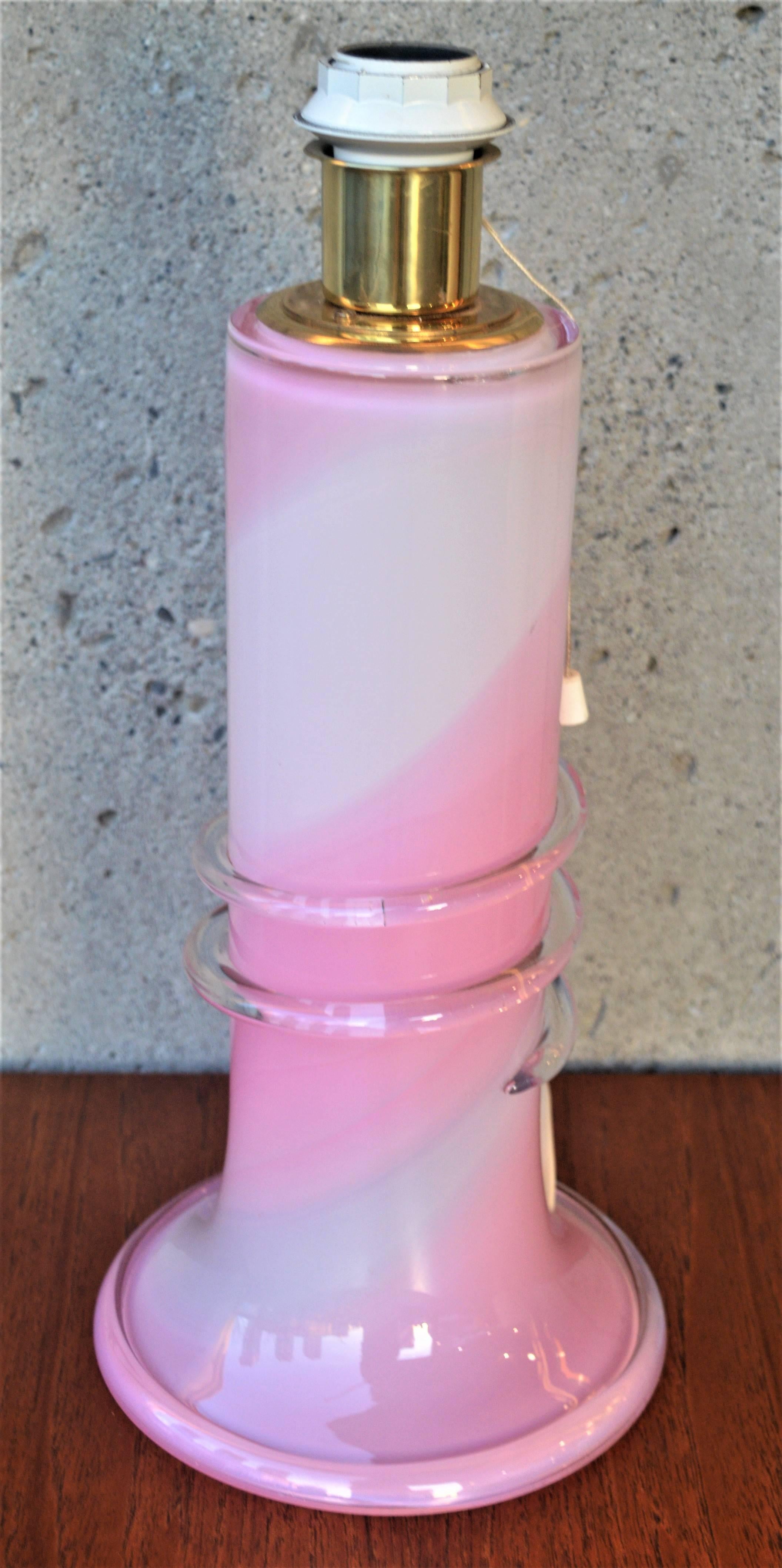 This is a spectacular example of the Lyktan glass in swirls of pink, white and clear and with an added swirl clear ribbon across the middle and a flared tulip base. Signed Studio Ahus Sweden 1985 and in amazing condition. Holds a standard base bulb