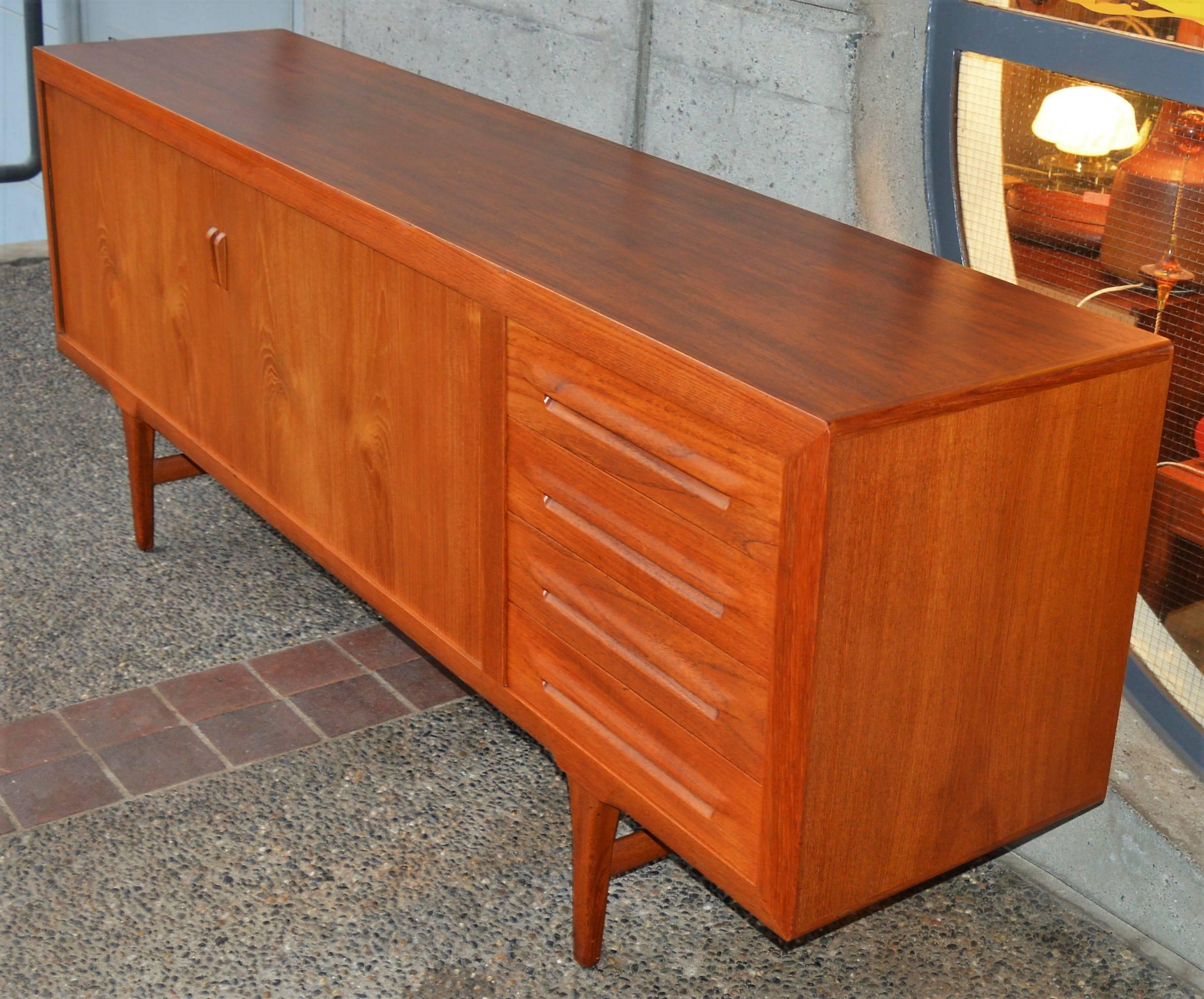 This absolutely impeccable, top quality Danish modern teak tambour credenza or buffet was designed by Ib Kofod Larsen in the 1950s. Featuring a mitred front edge molding detail that flares to meet the legs at the base, both on the front and back, an