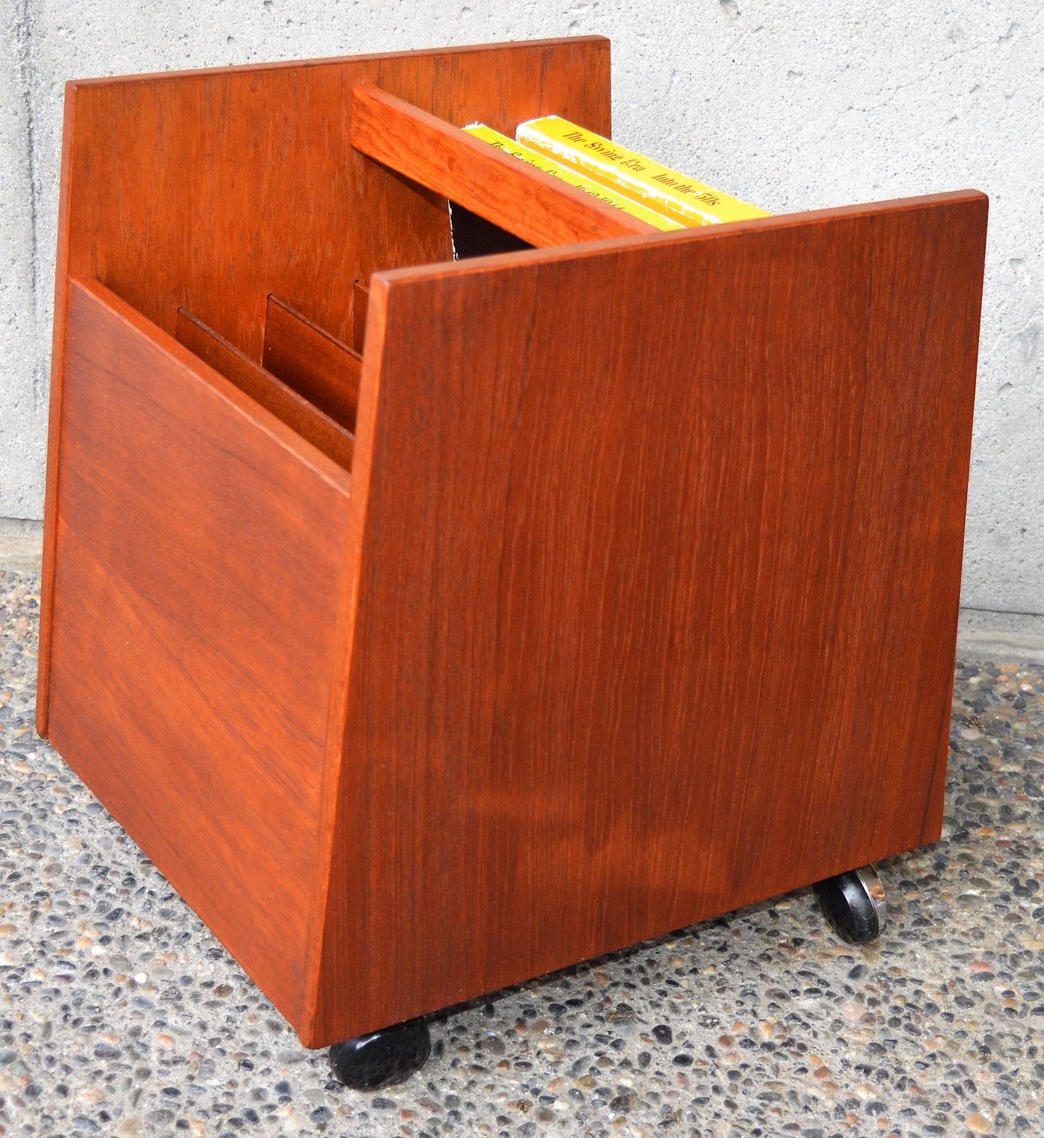 This super cool Danish modern teak LP cart holds likely 100 records/LPs or magazines and has trapezoidal flared sides and a cubic look from the front. The handy handle and casters make it super easy to move around. In fabulous condition and made by