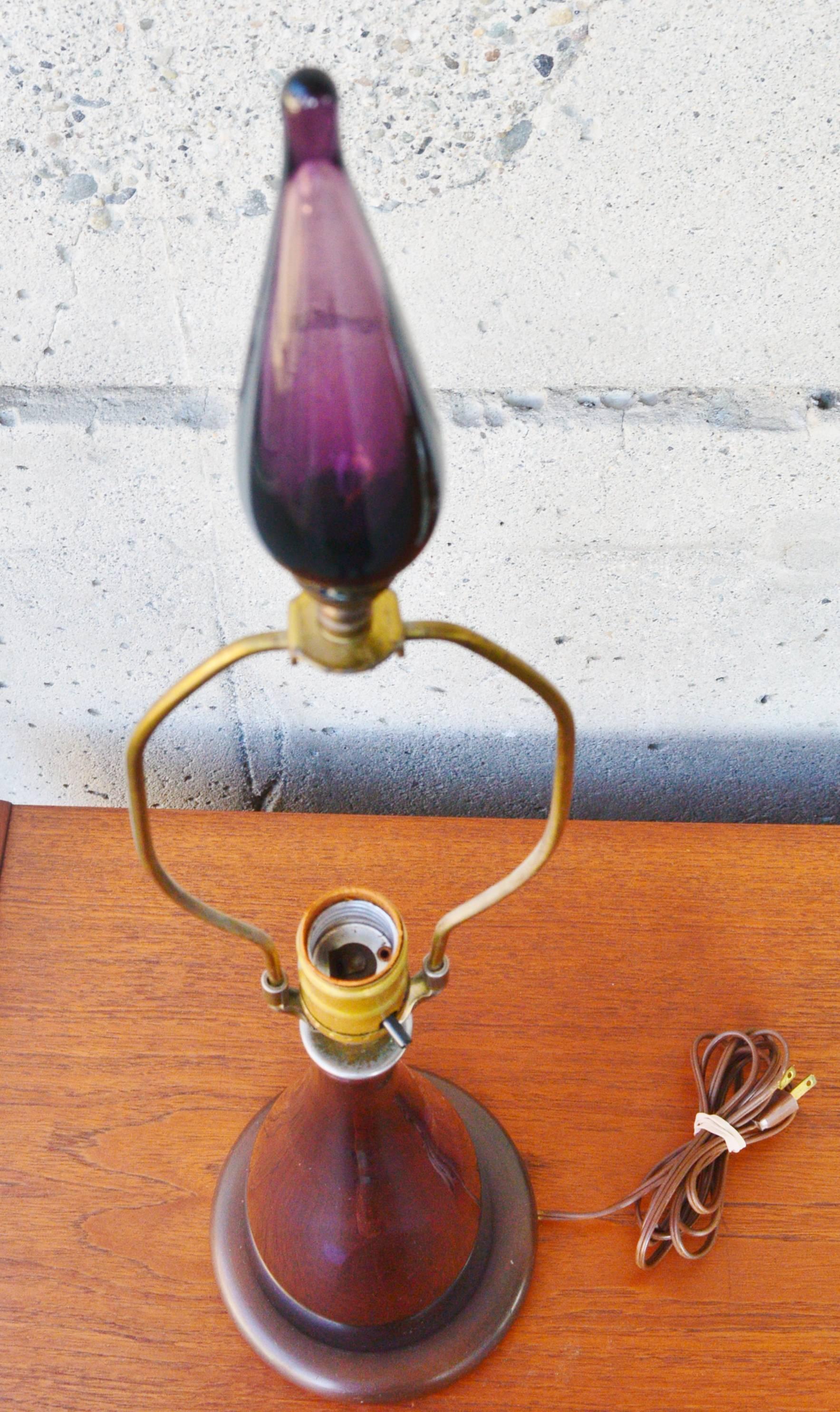This gorgeous Mid-Century Modern wine bottle shaped Blenko handblown glass lamp is in a rare shade of amethyst and includes the original tear-drop shaped finial and harp and circular wood base. In excellent condition except for wear to the metal CAP