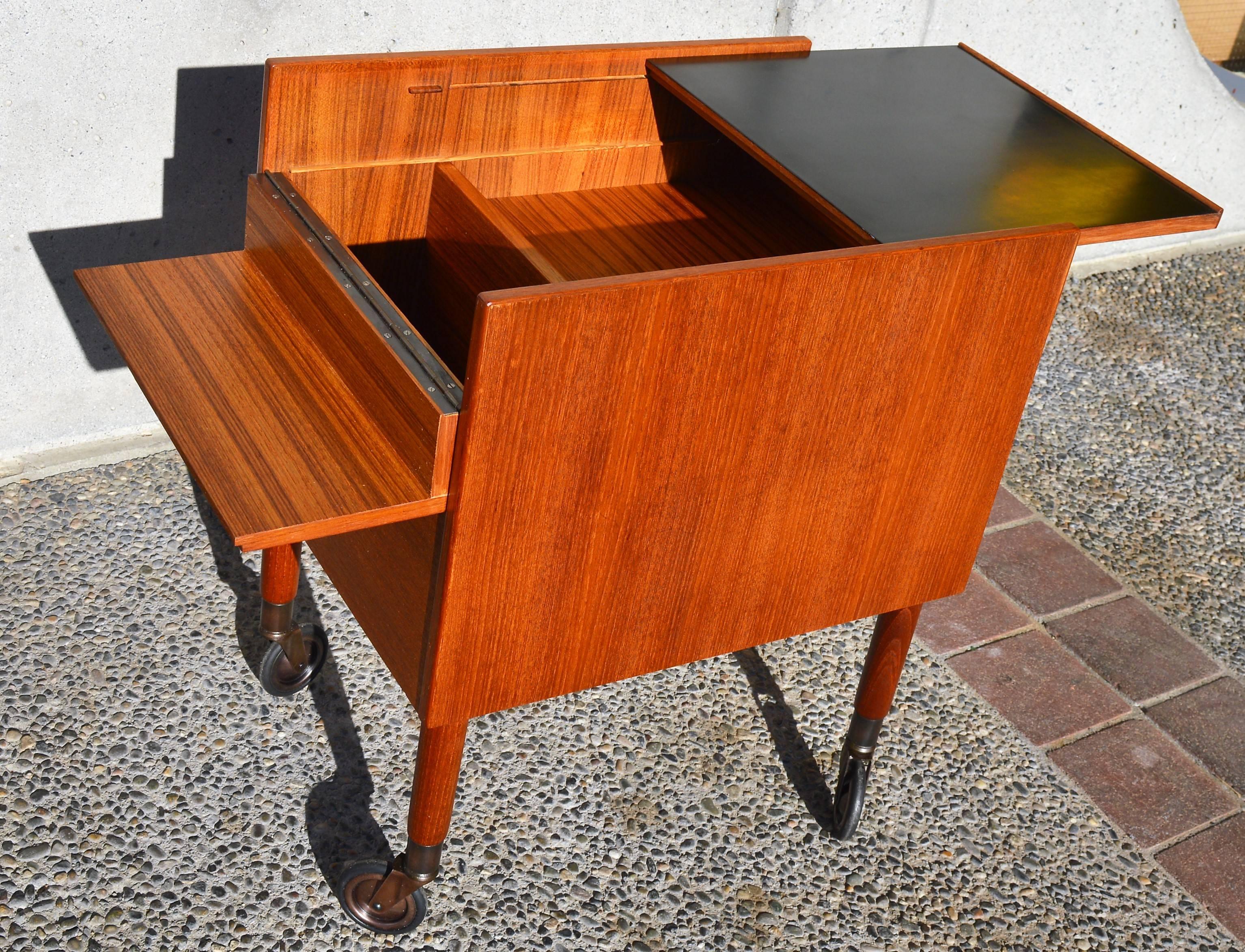 This super unique Scandinavian teak side table, storage cart, file cabinet or bar on copper casters has hidden storage inside. Slide the black laminate surface forward and flip open the back section which has a brass piano hinge to access the