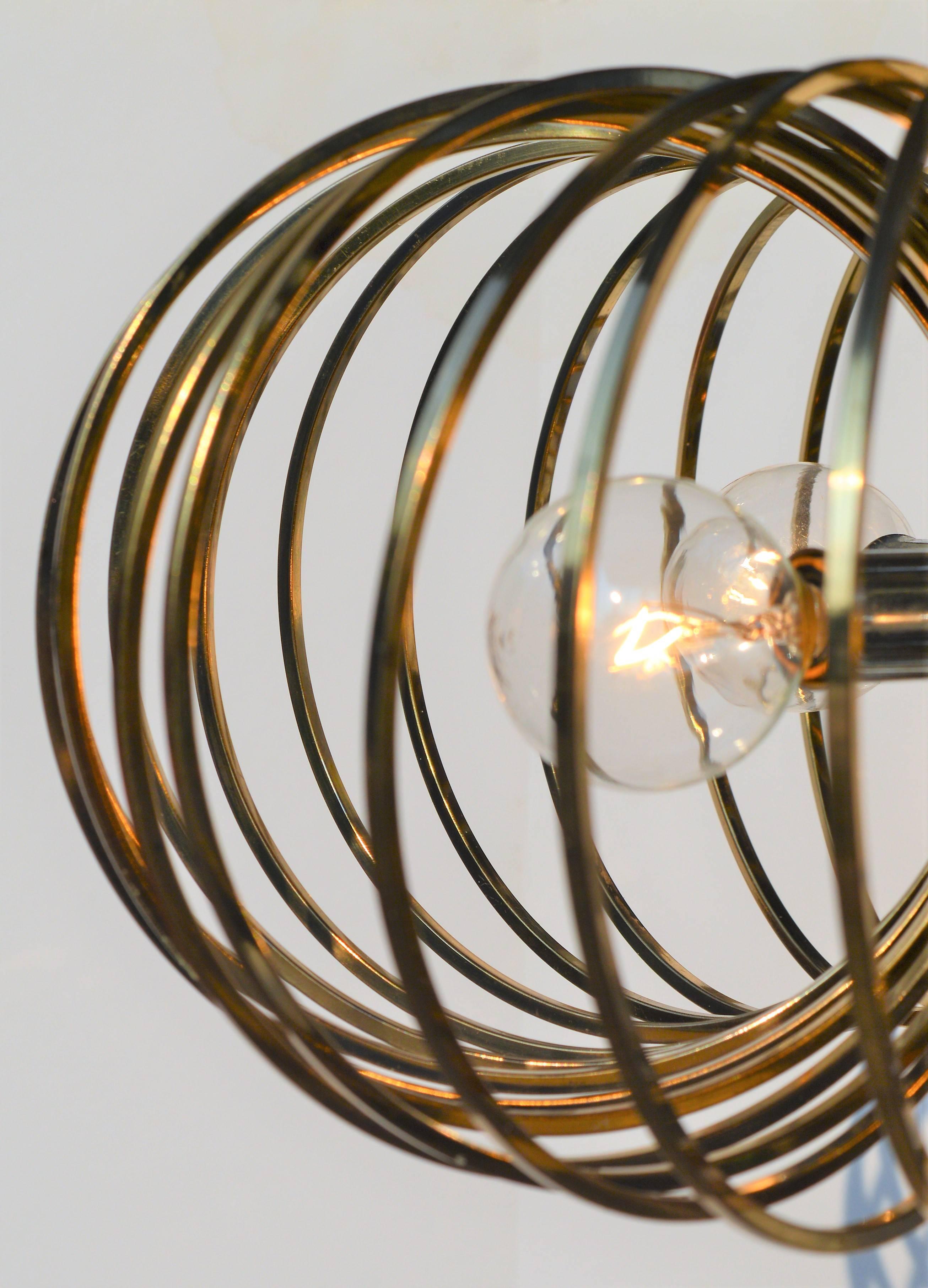 This striking pendant light or chandelier was designed in the 1960s by Sciolari for Lightolier and is playfully reminiscent of the Slinky toy of our childhoods. Featuring brass rings that encircle a central chrome band with four lights. The brass is