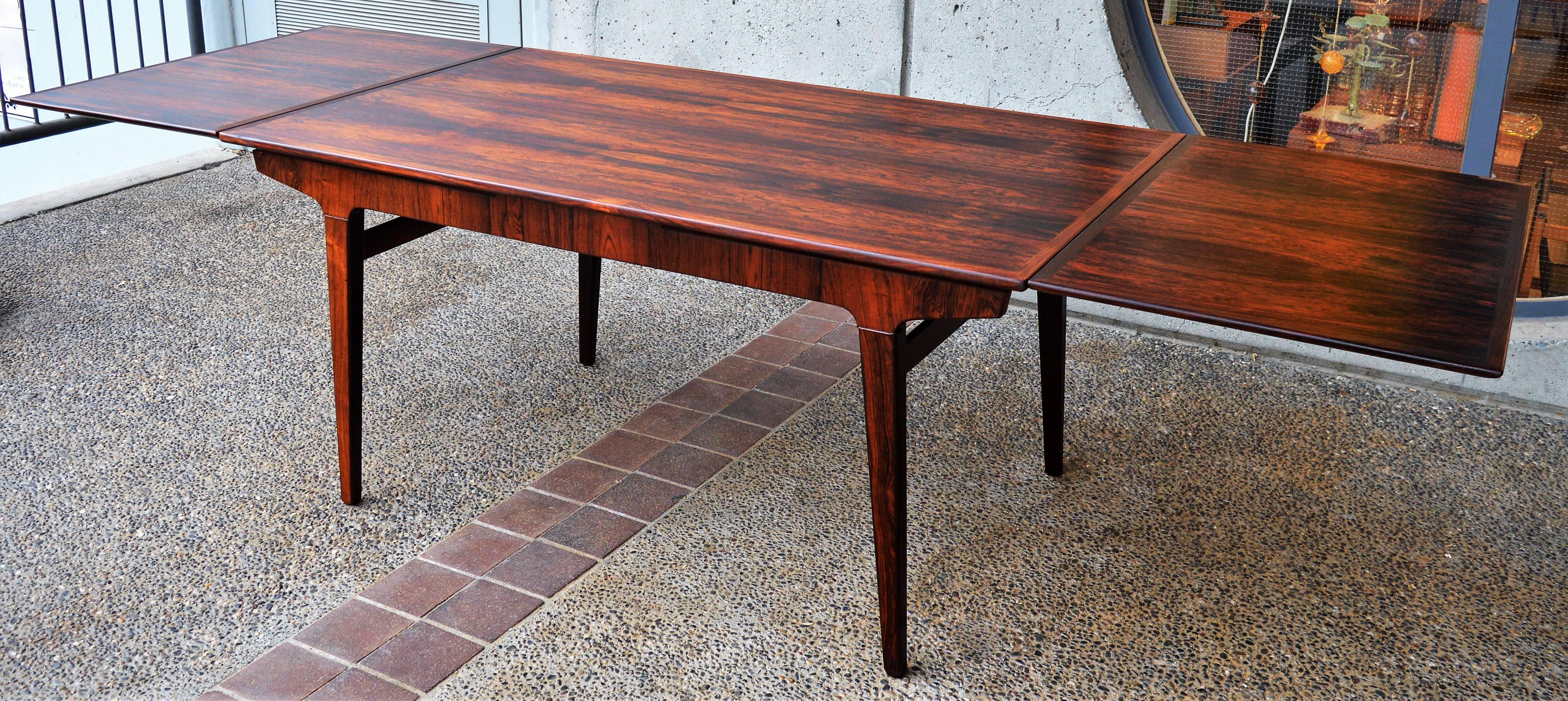 This amazing Danish modern rosewood dining table by Johannes Andersen, features his iconic splayed legs that melds into the sculptural table apron - in this version with a subtle wood ring at the top of the legs. The contouring of the apron, the