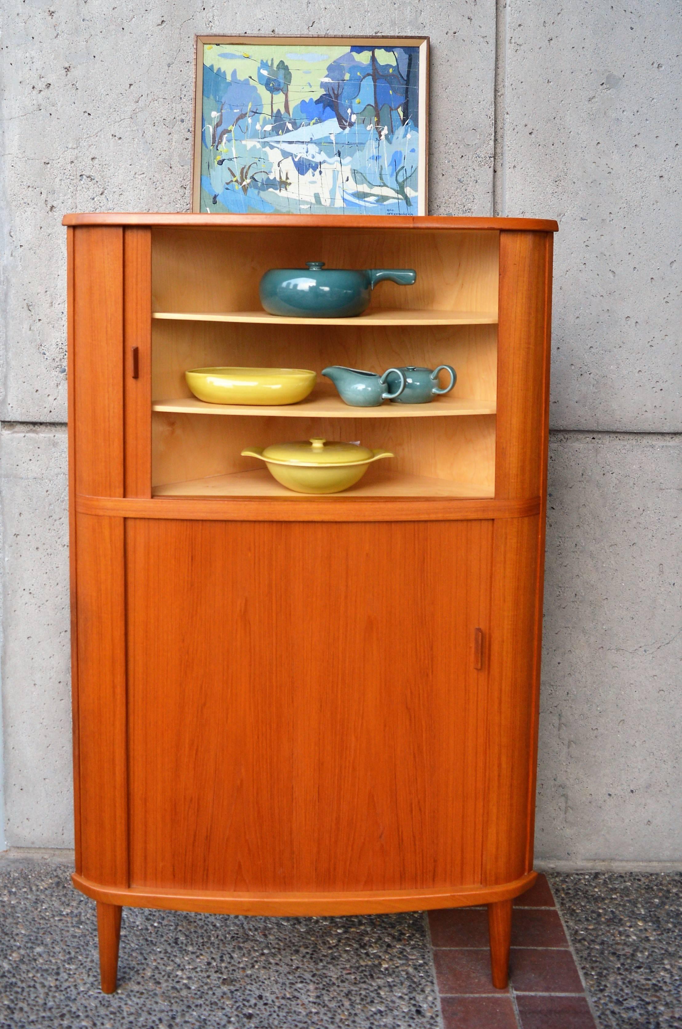 This rare Danish modern three-legged corner cabinet is a quality, all wood construction by Skovmand & Andersen of Denmark, 1960s. The book-matched grain to the teak upper and lower tamboured doors, the subtly curved front and the finish detailing