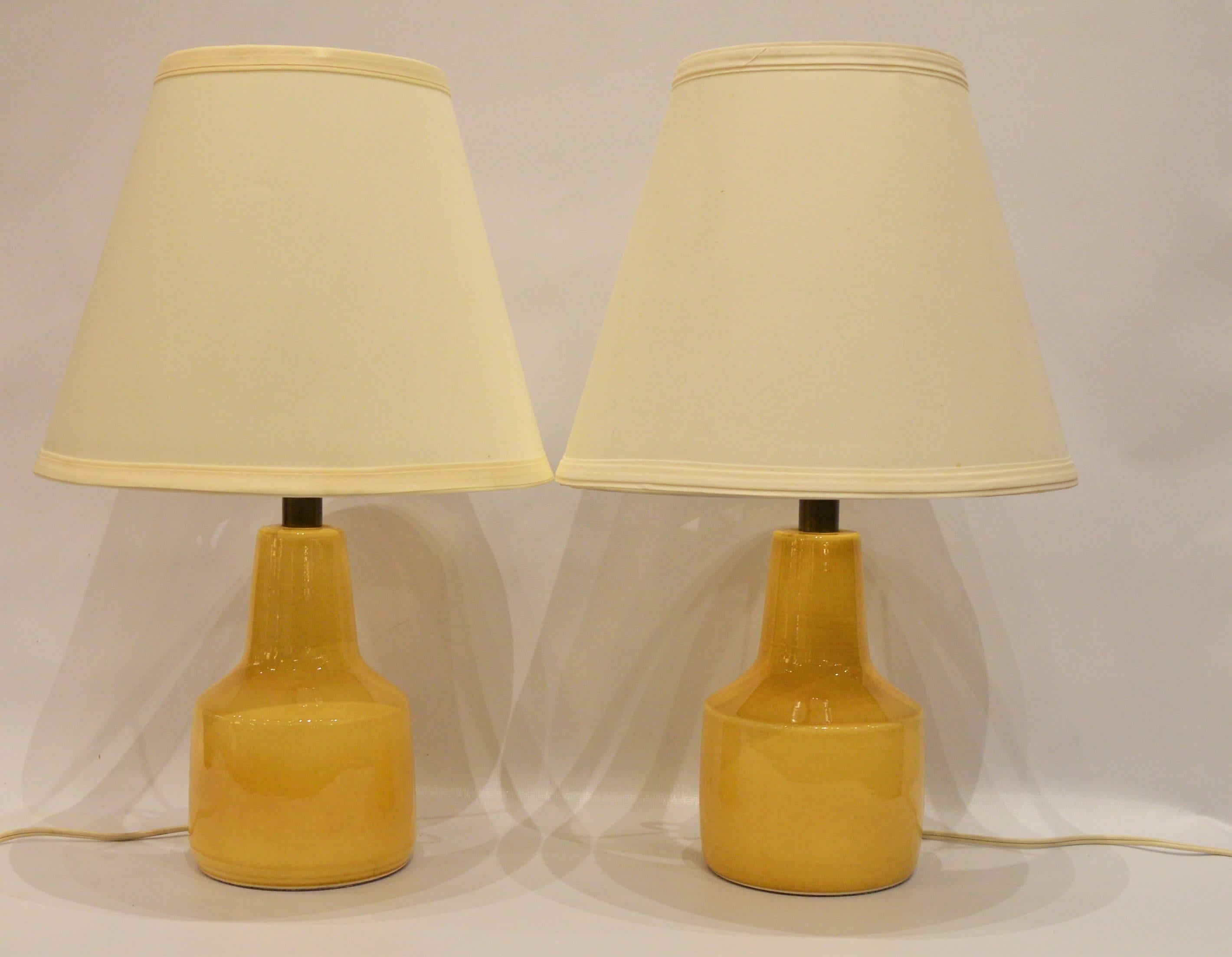 This lovely pair of soft yellow compact ceramic lamps were made by Lotte and Gunnar Bostlund and are the perfect size for compact bedside lamps. Paired with conical white/off-white lamp shades, though one has a spot that can be turned to the back.
