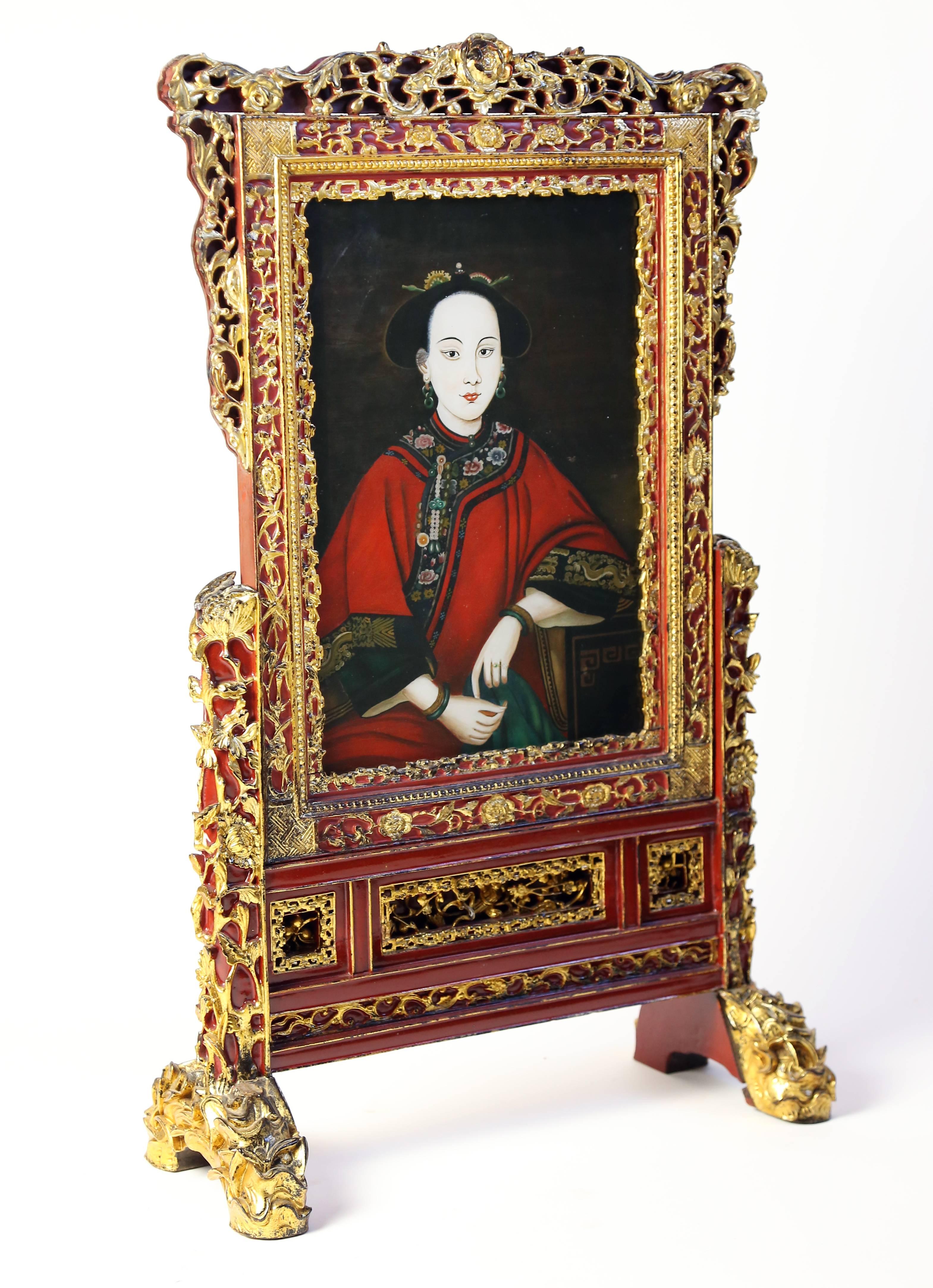An ornate and unusual table screen featuring a fantastic reverse glass painted portrait of a beautiful young woman. Portrait is set into a highly carved and decorative gilded frame and stand.
 