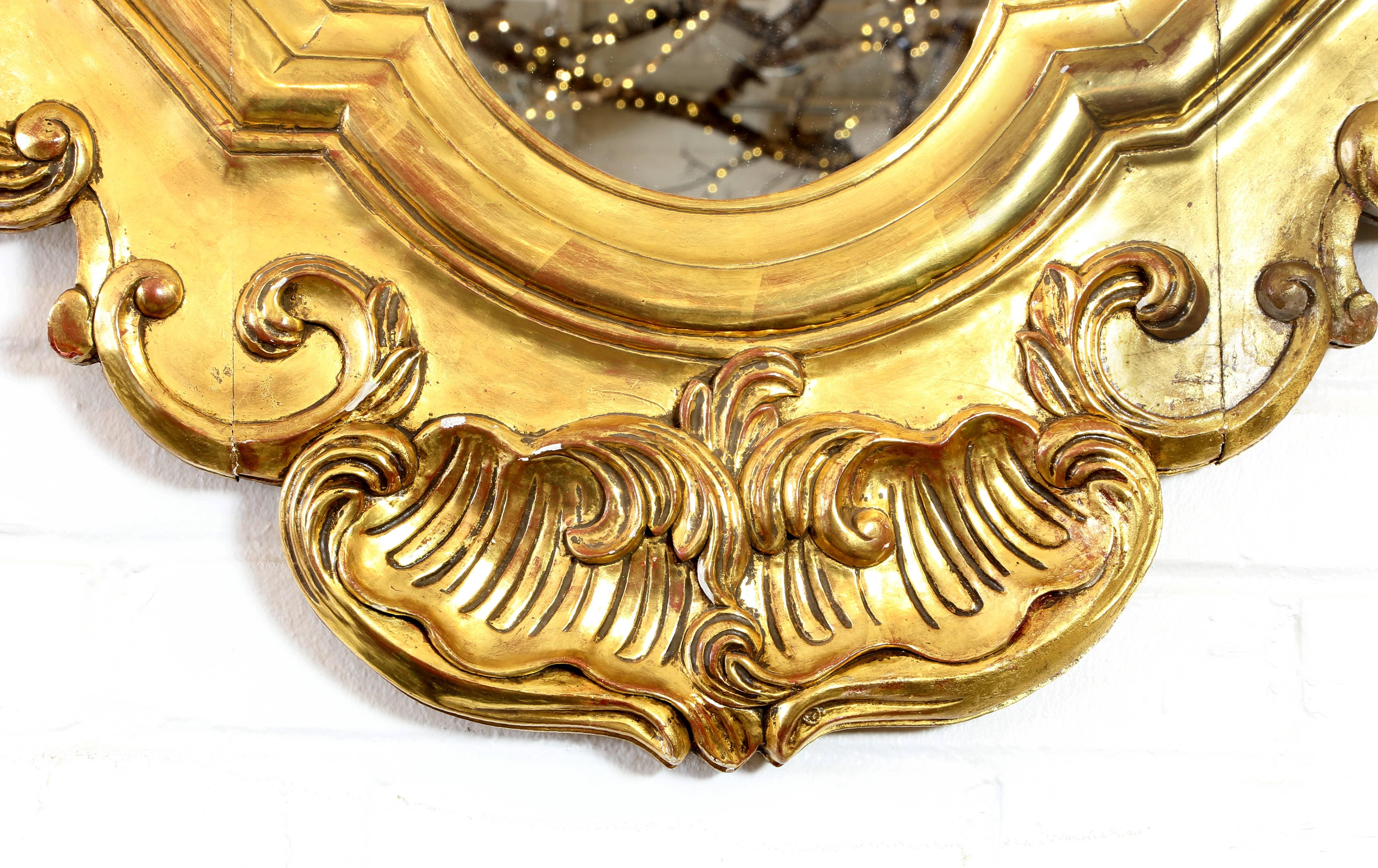 Italian giltwood wall mirror, the shaped carved frame of scrolls and floral motif, flower crested top, encasing flat mirror plate, intact with minor repairs, minor gilt loss.
     