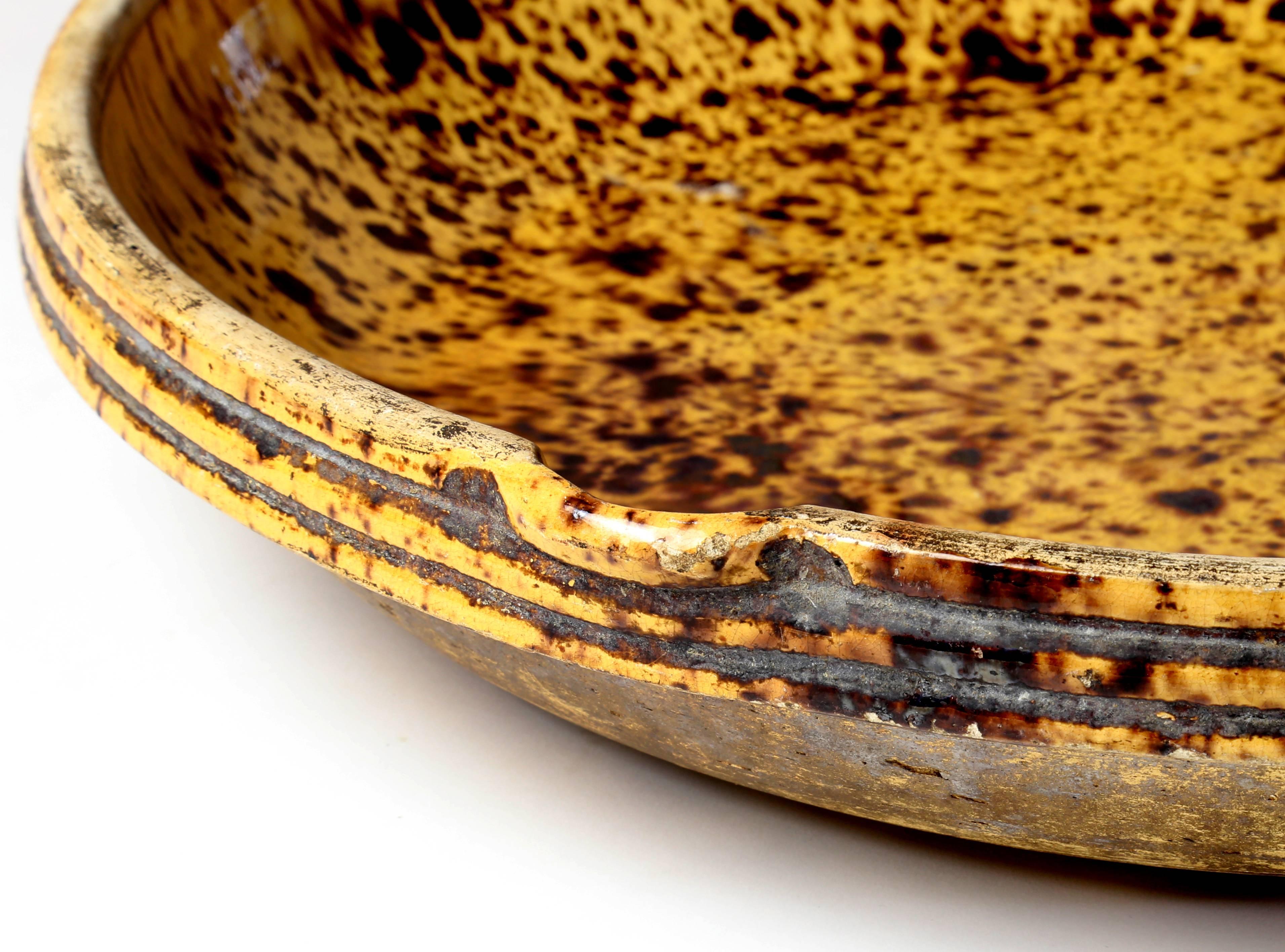A large round antique terracotta cheese draining bowl with a gold and brown speckled glaze.