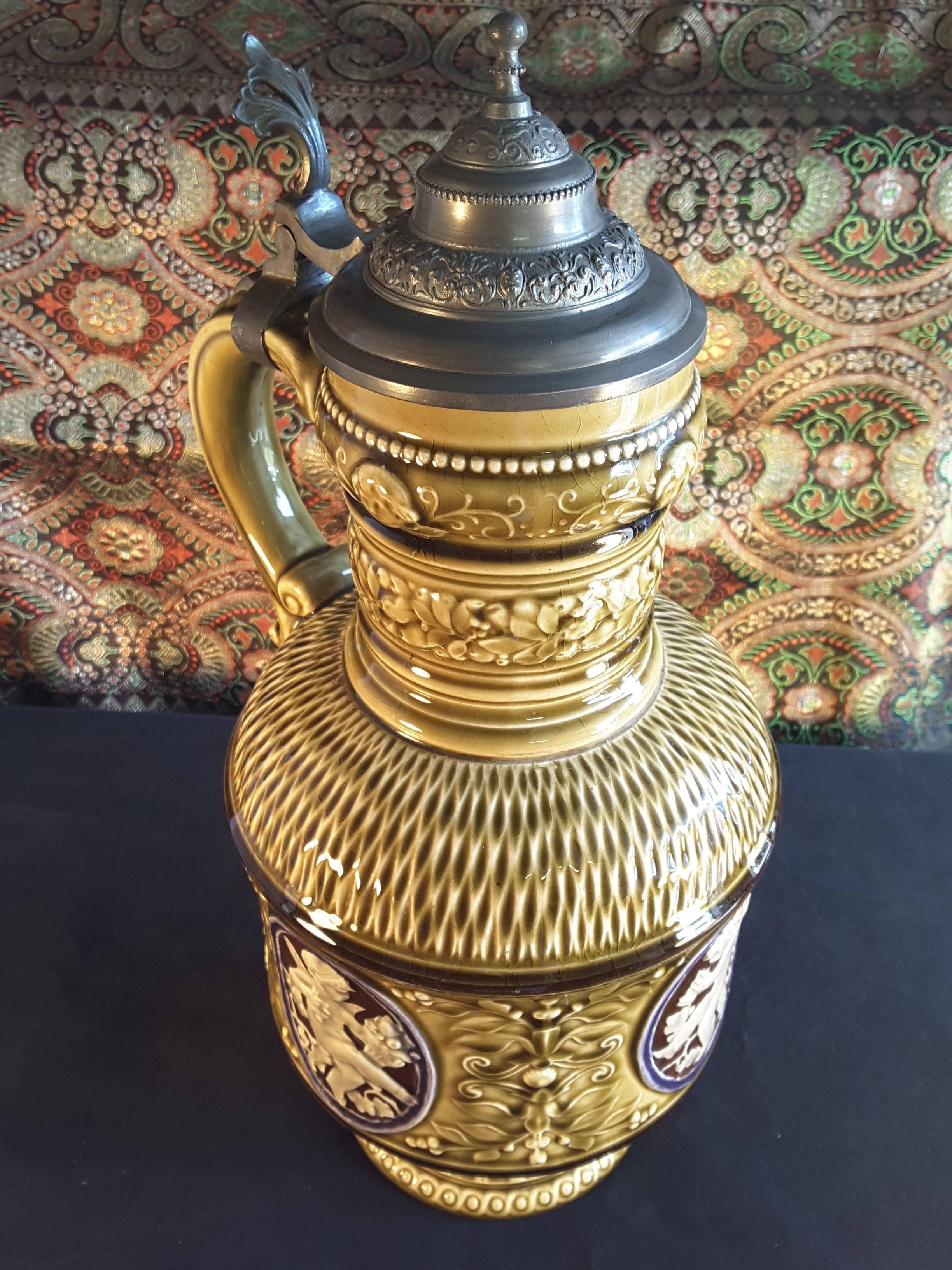 Caraffa da vino in stile rinascimentale montata su peltro, con smalto verde oliva e quattro cartigli ovali con cornice blu raffiguranti Bacco bambino in crema su sfondo marrone.
Marchio circolare impresso sulla base, probabilmente austriaco, circa