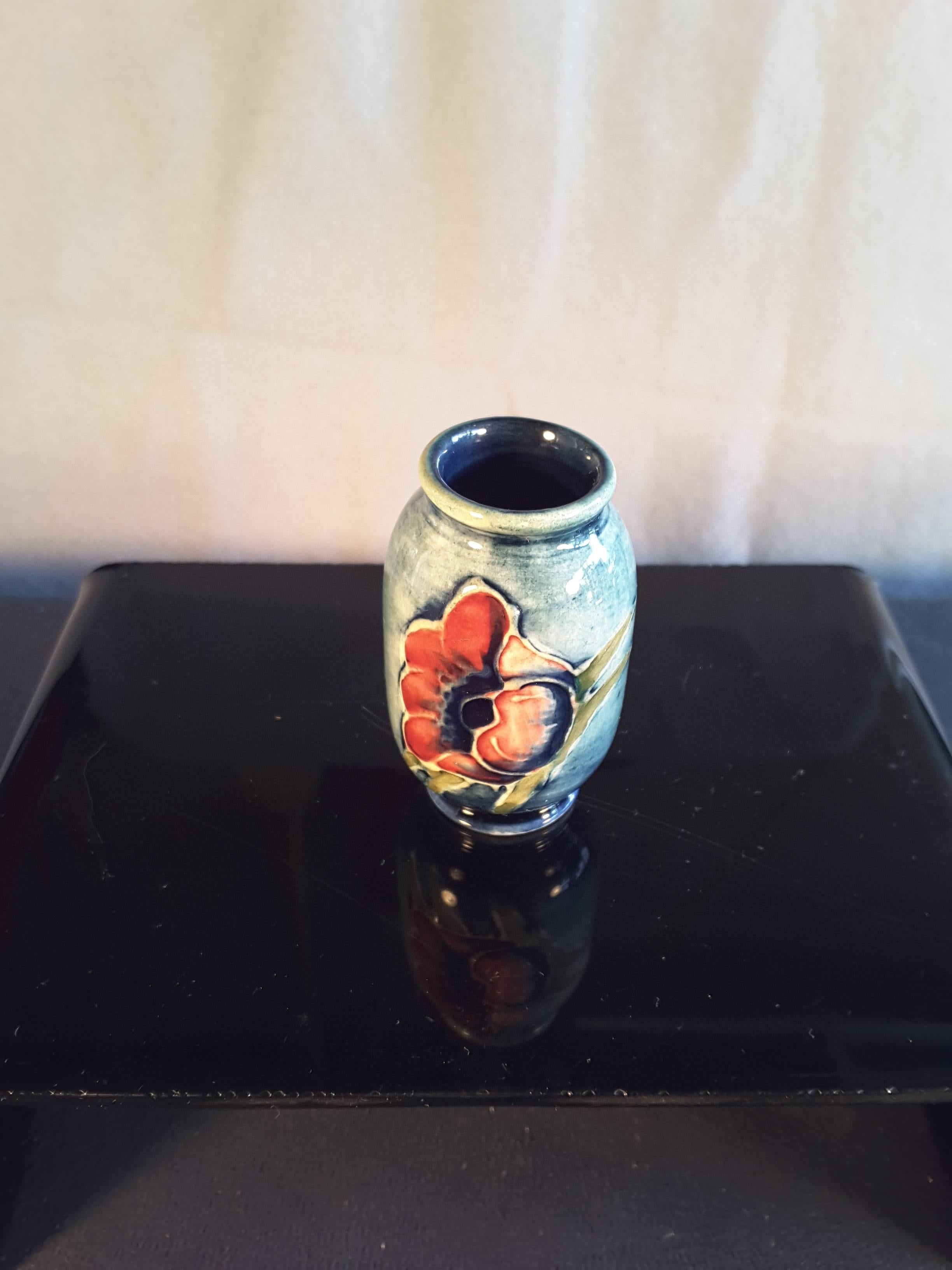Un bel vaso Moorcroft in miniatura, prodotto in Inghilterra, con disegno floreale. Il vaso ha un tipico sfondo blu con due fiori su entrambi i lati. Il fondo è contrassegnato dalla scritta Moorcroft Made in England. Il vaso misura 2 1/8