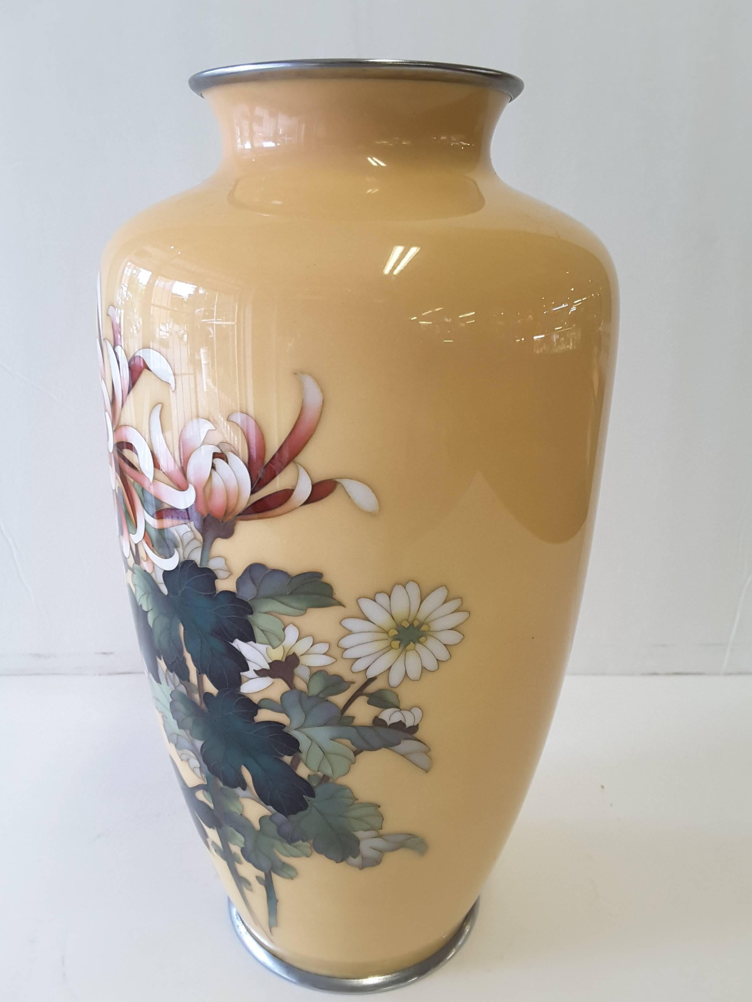A Japanese cloisonne enamel vase by Ando Jubei (1876-1953), Meiji period vase. An early 20th century enamel worked in silver wire decorated with stalks of flowering spider chrysanthemums on a peach colored background. The top and base each have a