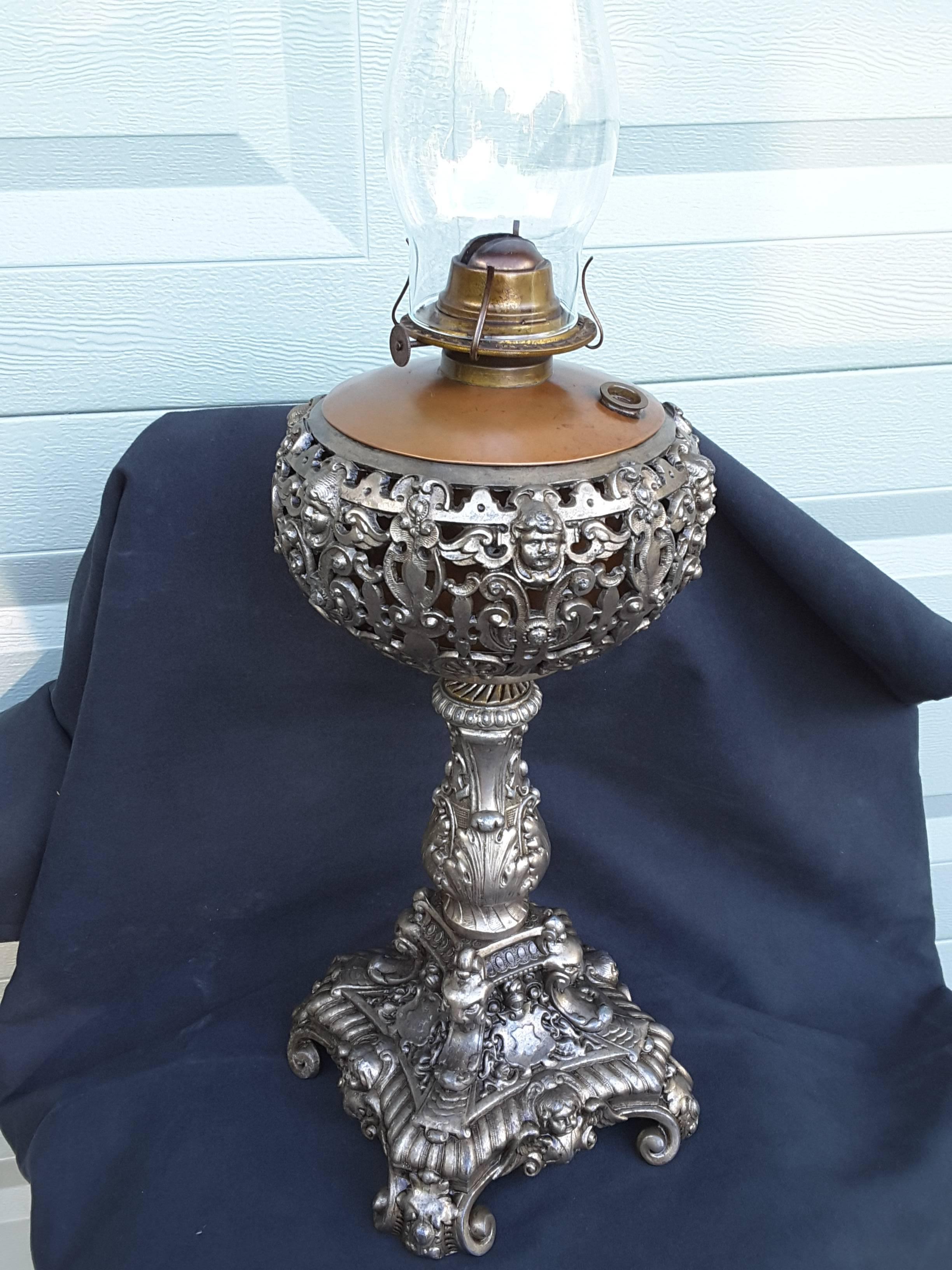 Angel face with wings oil lamp, silver tone finish, scrolled foot and acanthus leaf decoration. The kerosene pot is made of copper and a brass burner, still functions as an oil lamp and has not been drilled for a lamp. The lamp measures 17